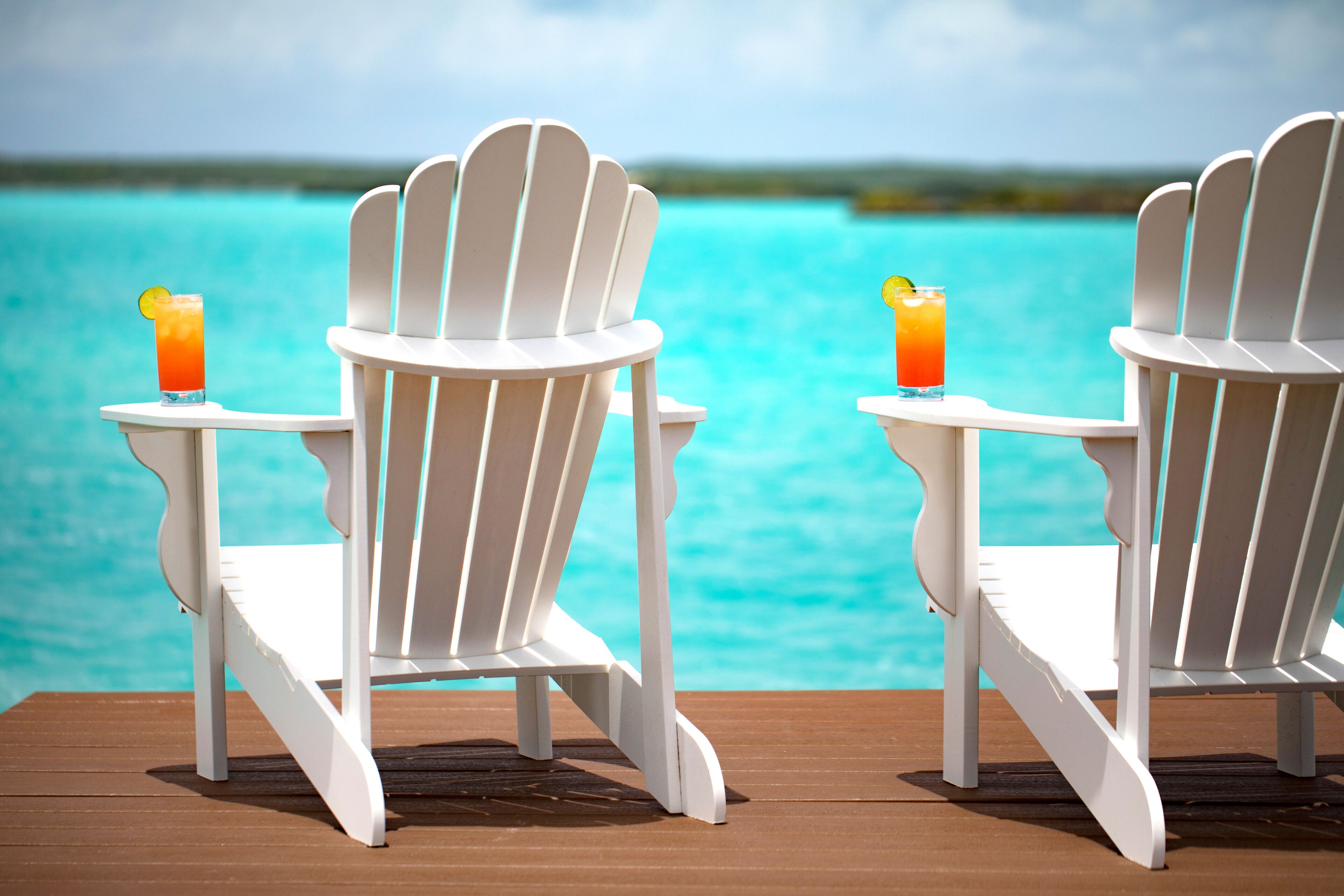 Two white chairs and two drinks on a deck at the Chalk Sound lagoon.