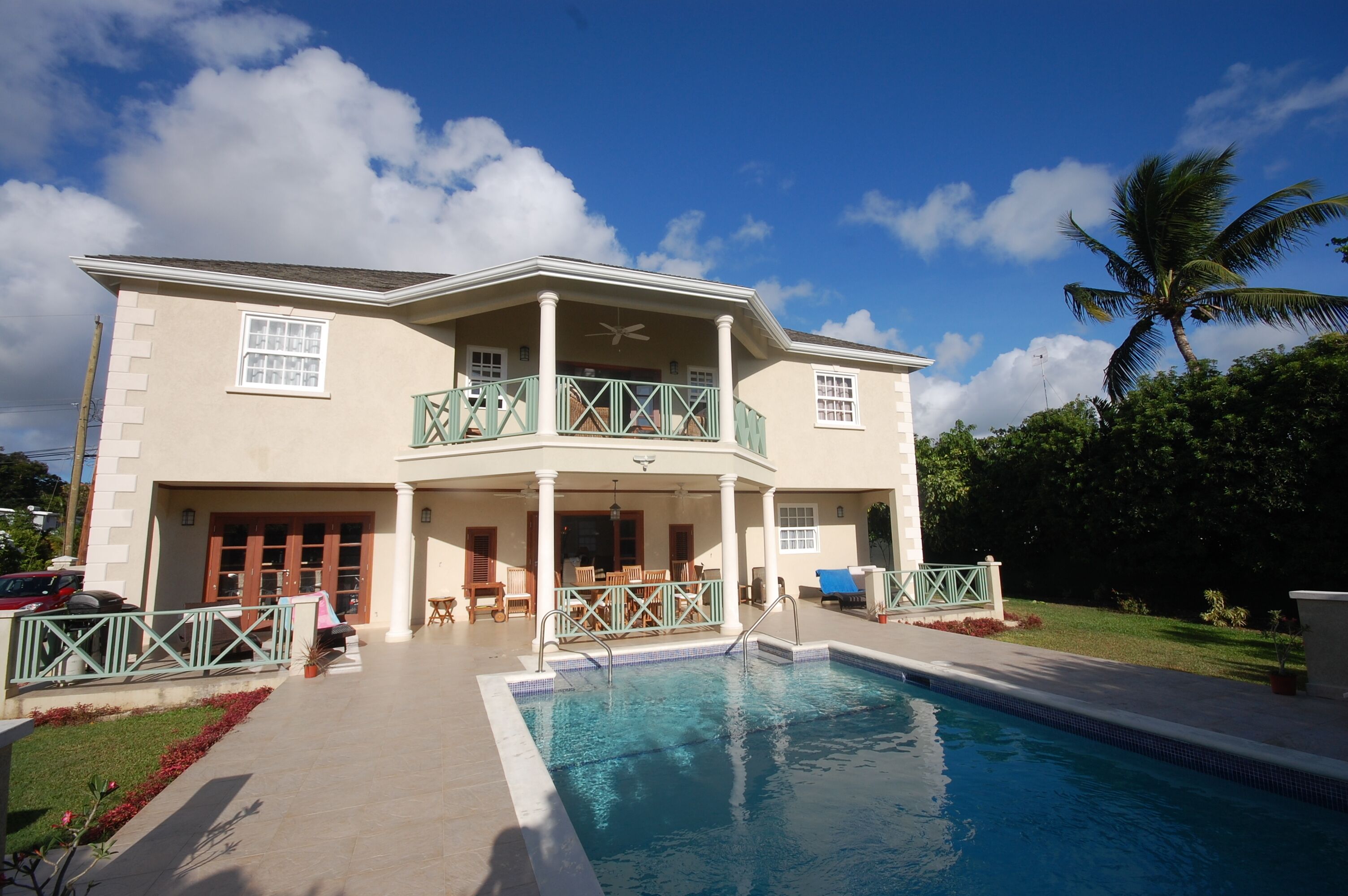 The pool and the rear of the villa on a clear day, with a palm tree at the side of the garden.
