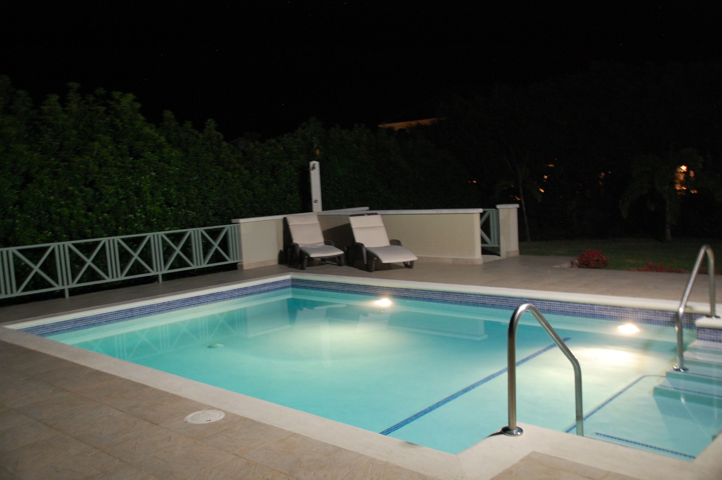 The pool at night, with underwater lights and two sun loungers on the deck.