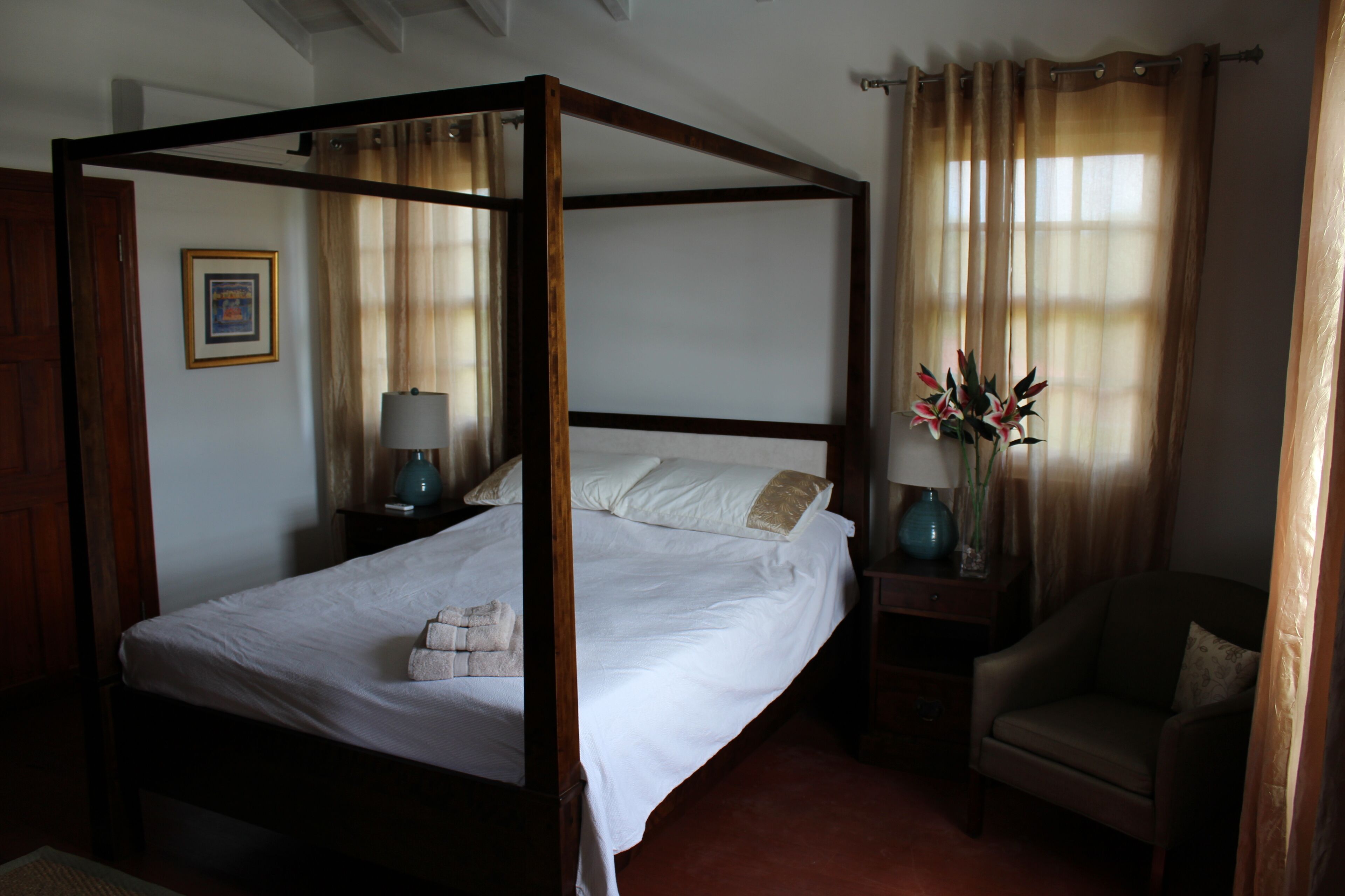 A bedroom with a four-poster bed, white bed linen, and folded towels.