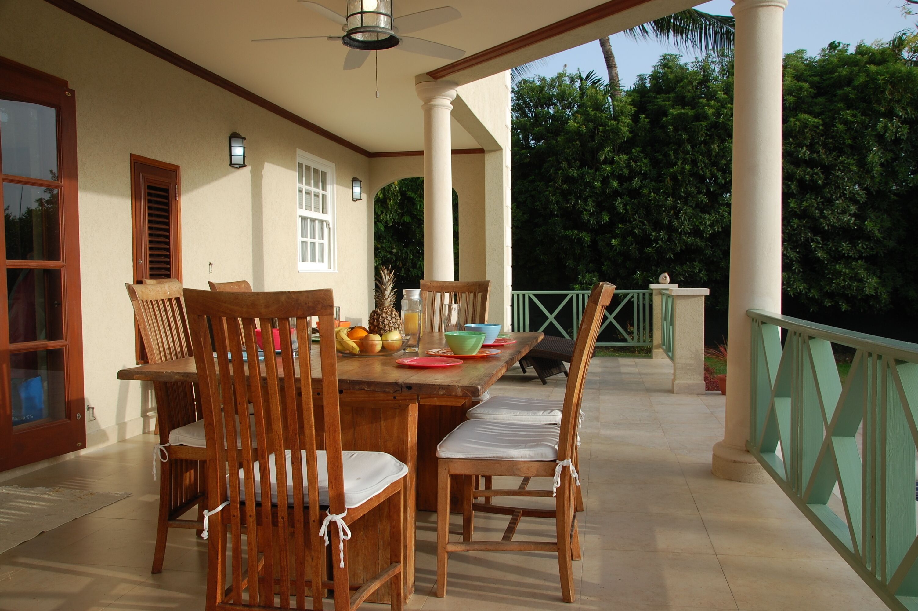 A wood dining table and chairs on the covered veranda, with fruit on the table.