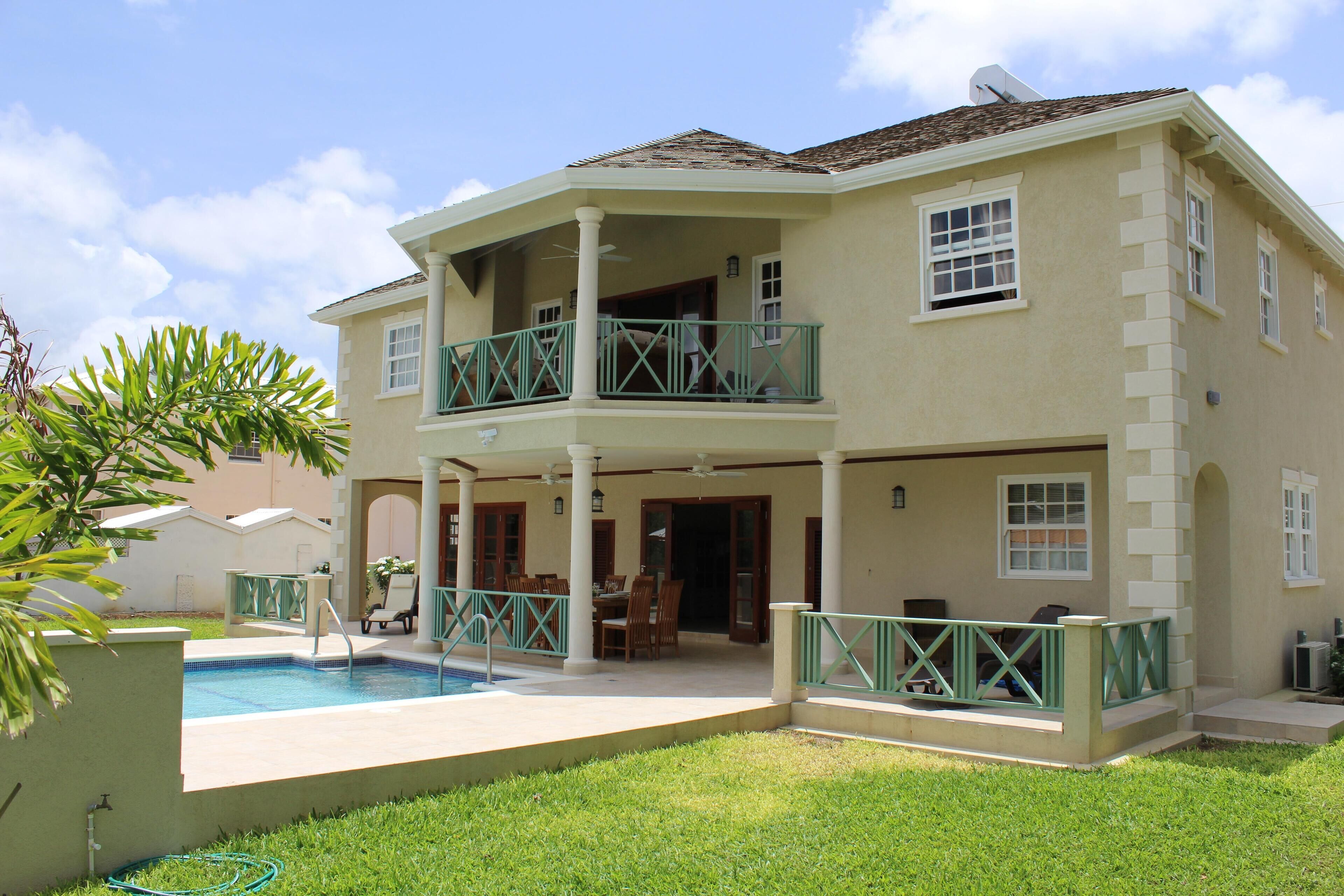 The rear of the villa in daylight, with the pool, the covered patio, and the upper balcony.