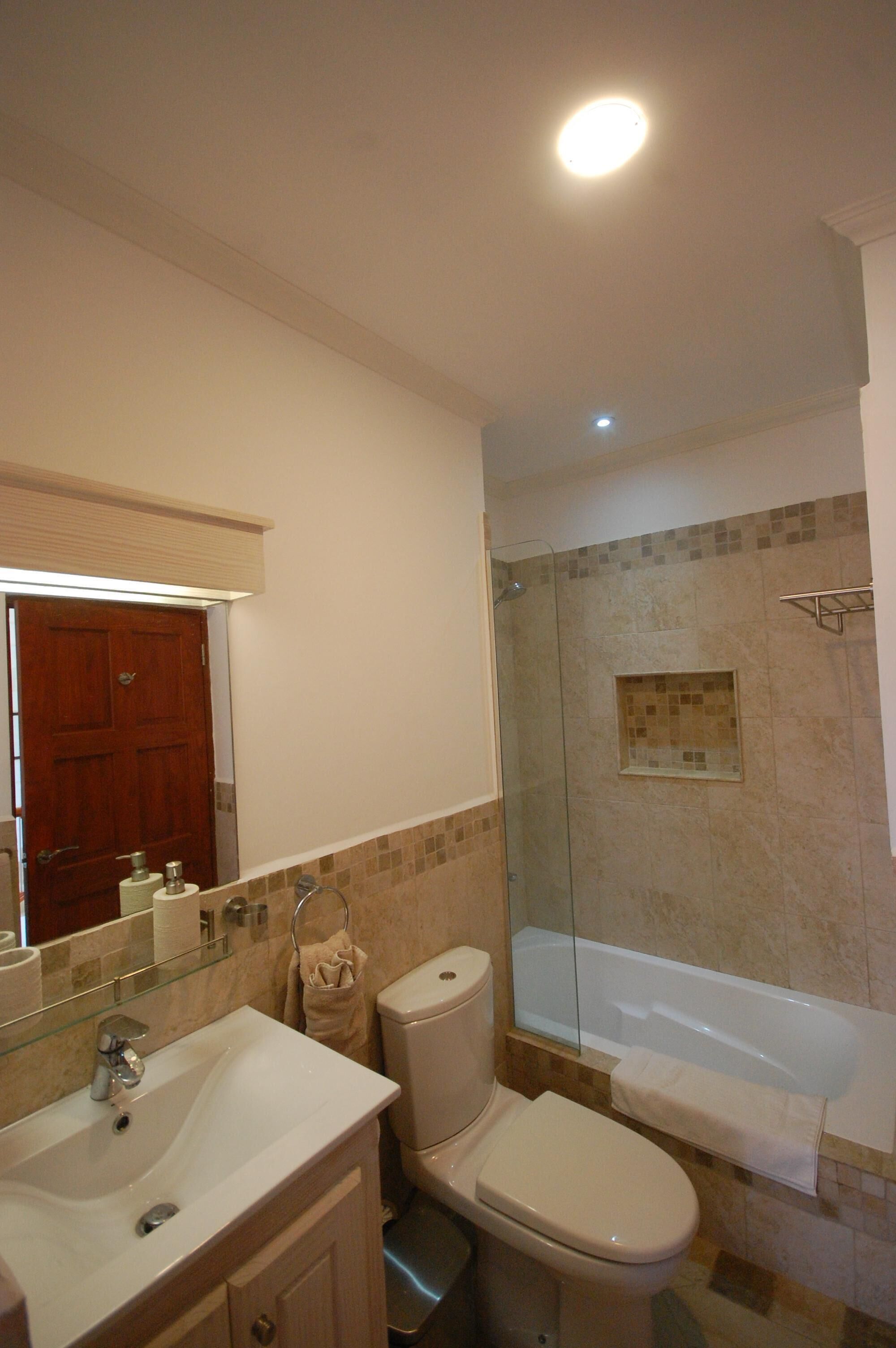 A bathroom with a sink, a toilet, and a bathtub with a glass shower screen.