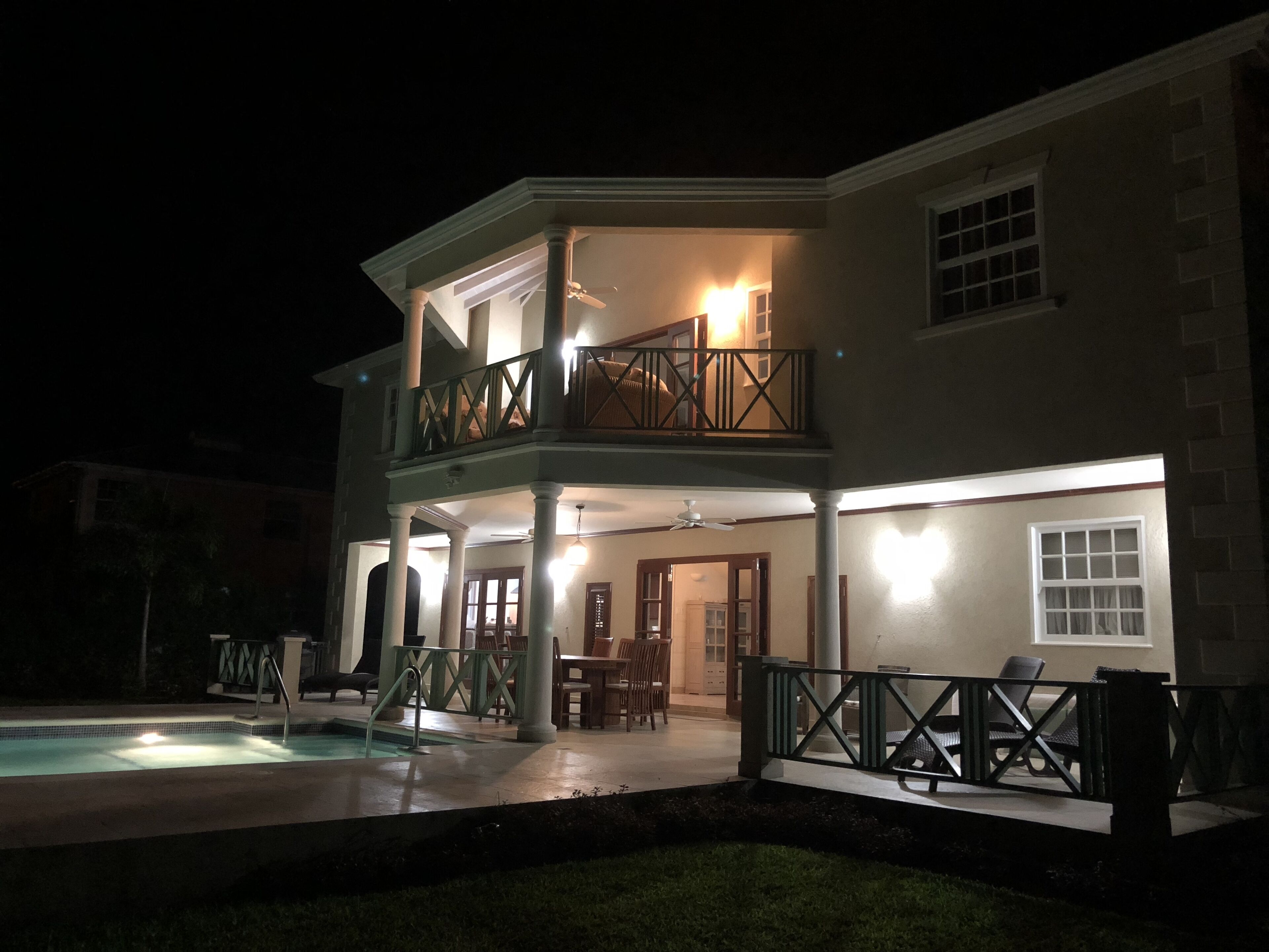 The rear of the villa at night, with lights on the patio and in the pool.