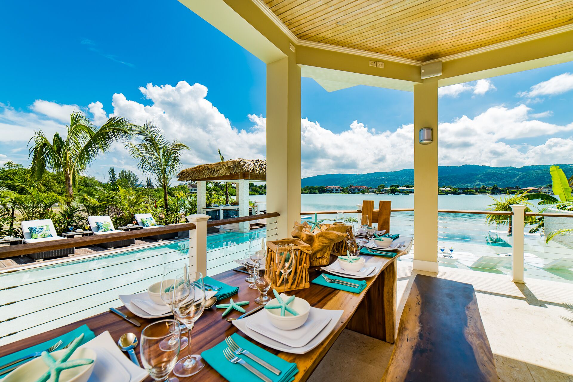 A covered terrace with a table set for a meal by the pool.