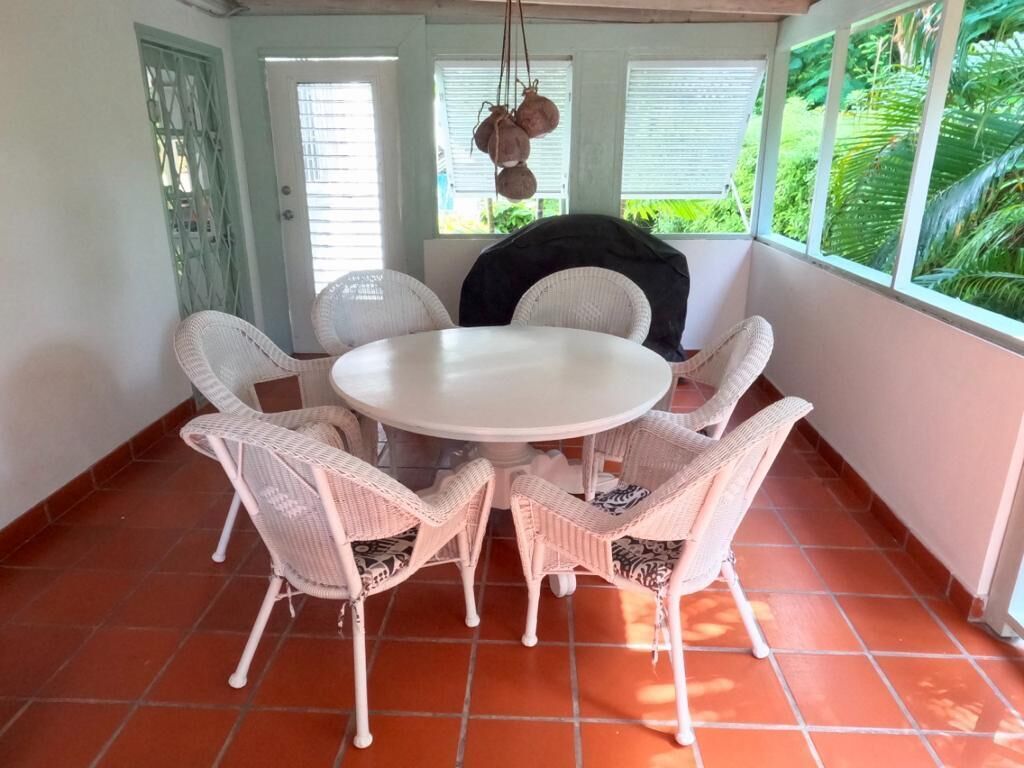 A veranda with a round table and six wicker chairs.