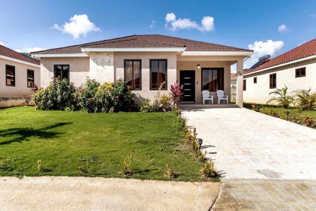 A one-story house with a lawn, shrubs, and a paved driveway.