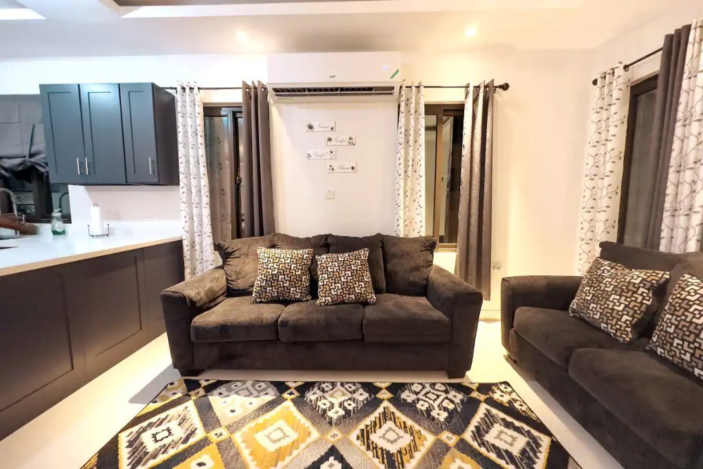 A living room with two brown sofas, a patterned rug, and a kitchen counter.
