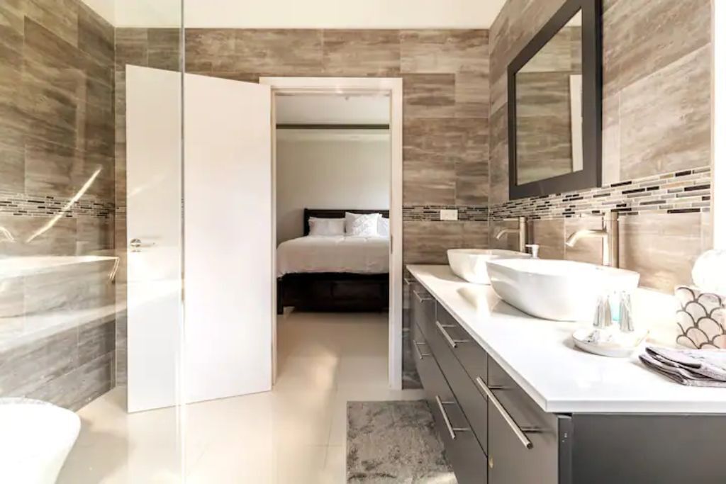 A bathroom with two sinks, a mirror, and a door to a bedroom.