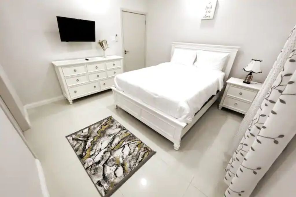 A bedroom with a double bed, a white dresser, and a wall-mounted television.