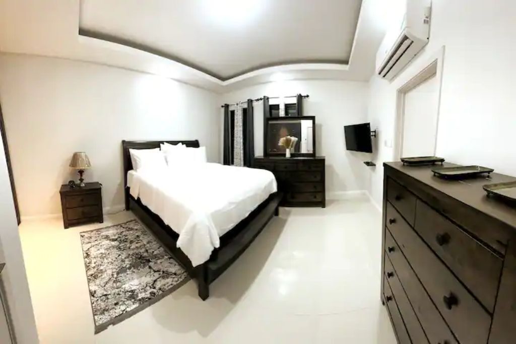 A bedroom with a double bed, two dark wood dressers, and an air conditioner.