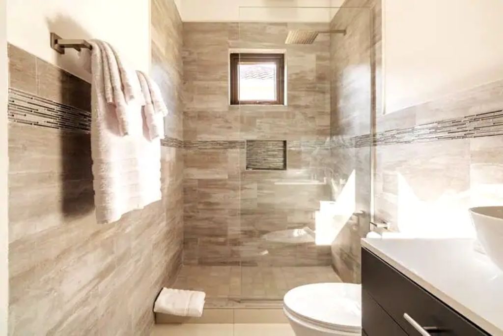 A bathroom with a glass shower, a toilet, and towels on a rail.