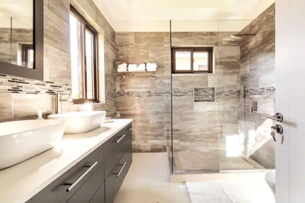 A bathroom with two sinks, a glass shower, and a window.