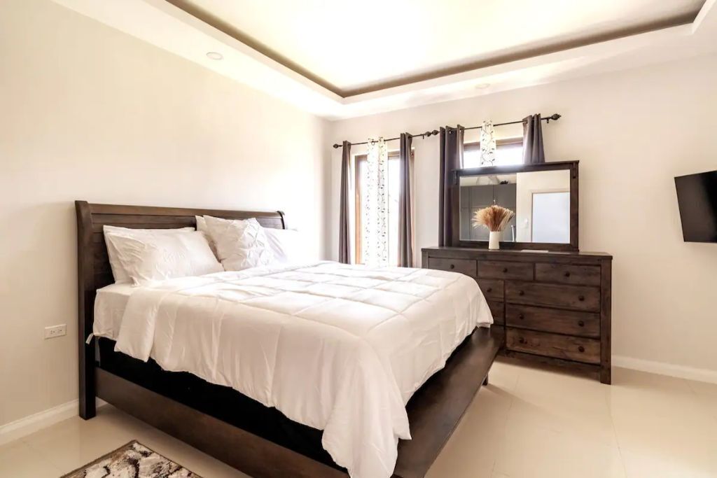 A bedroom with a double bed, a dresser with a mirror, and a wall-mounted television.