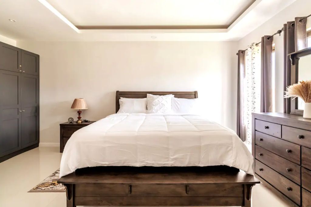 A bedroom with a double bed, a bench, a lamp, and a dresser.