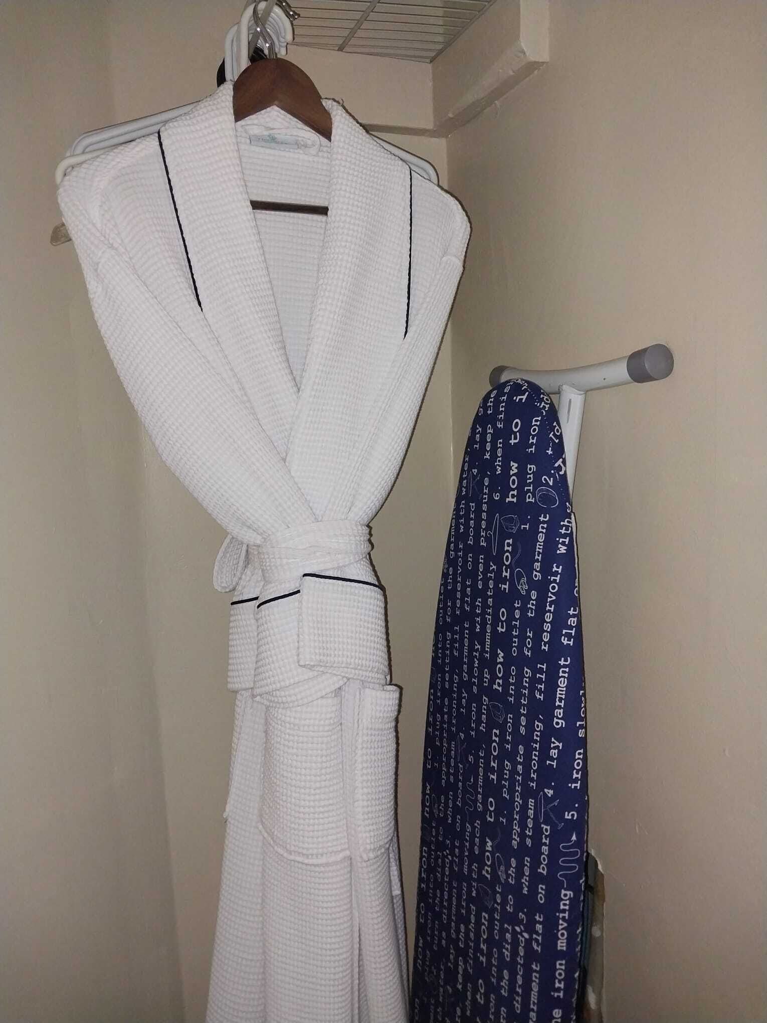 Robes and an ironing board in the closet.