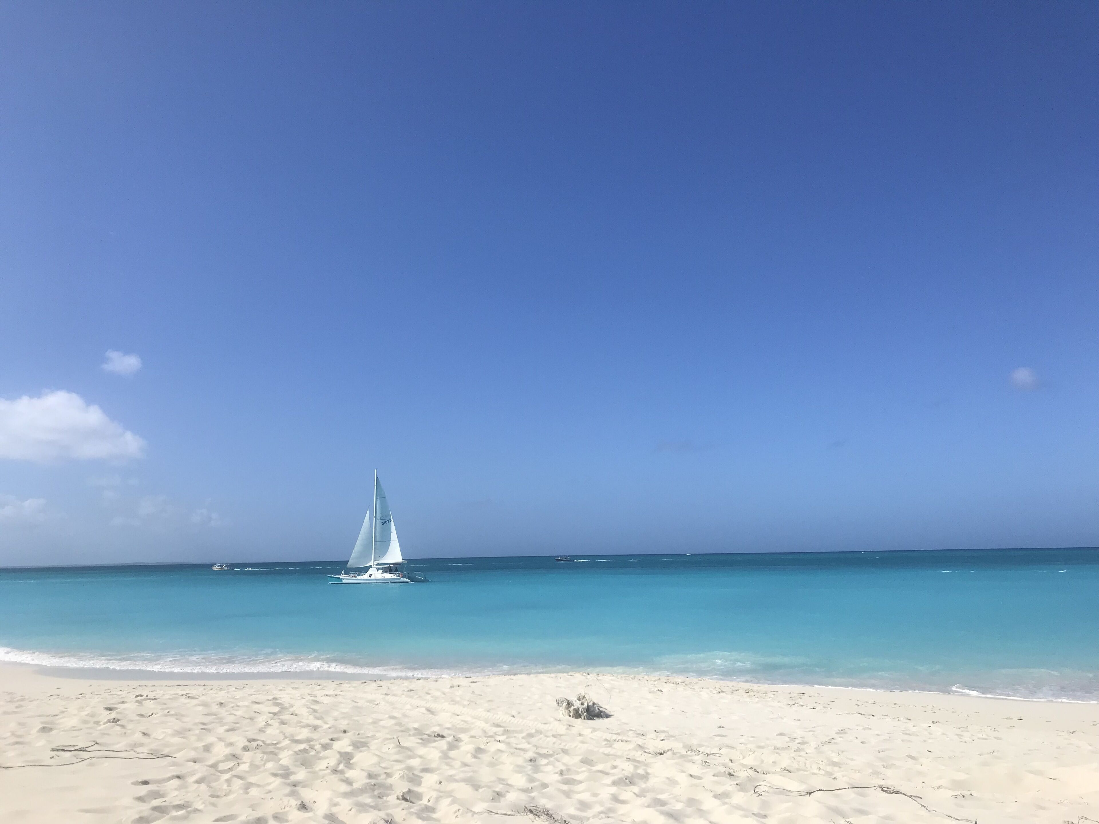 A sailboat on turquoise water at a white sand beach.