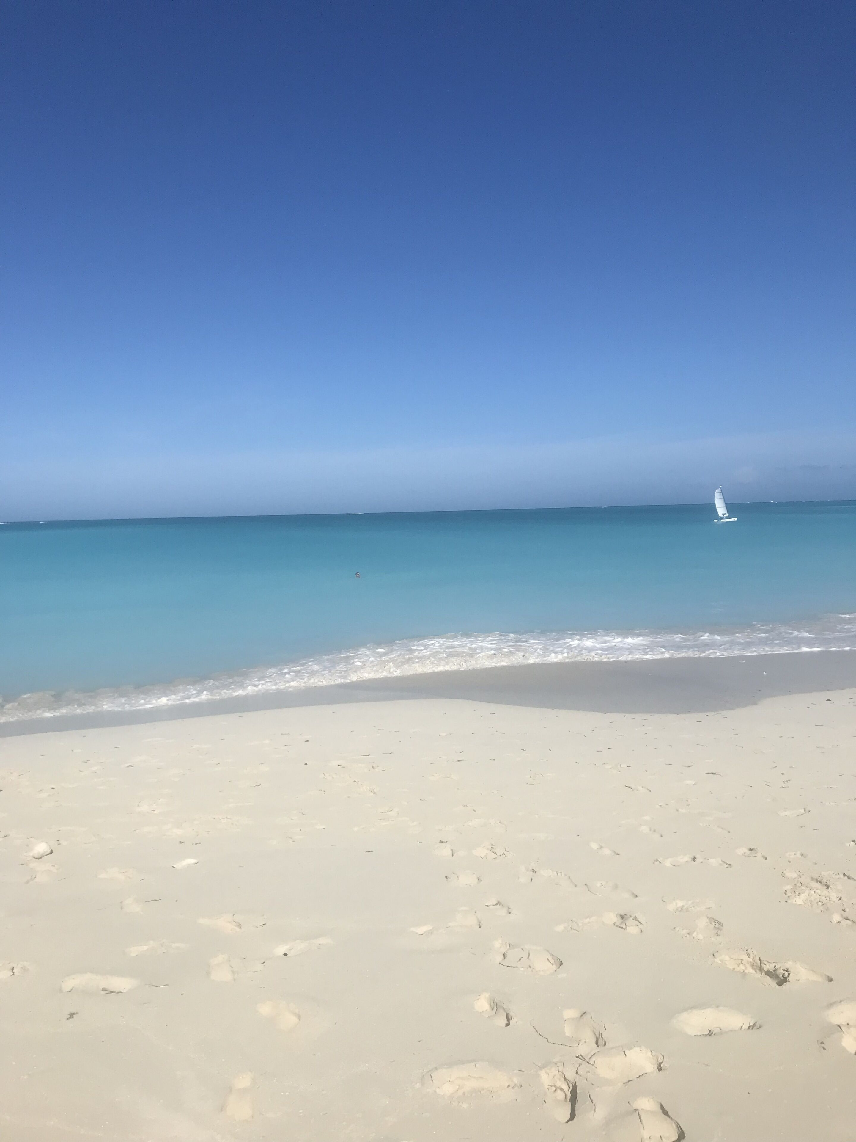 A white sand beach with a sailboat in the distance.