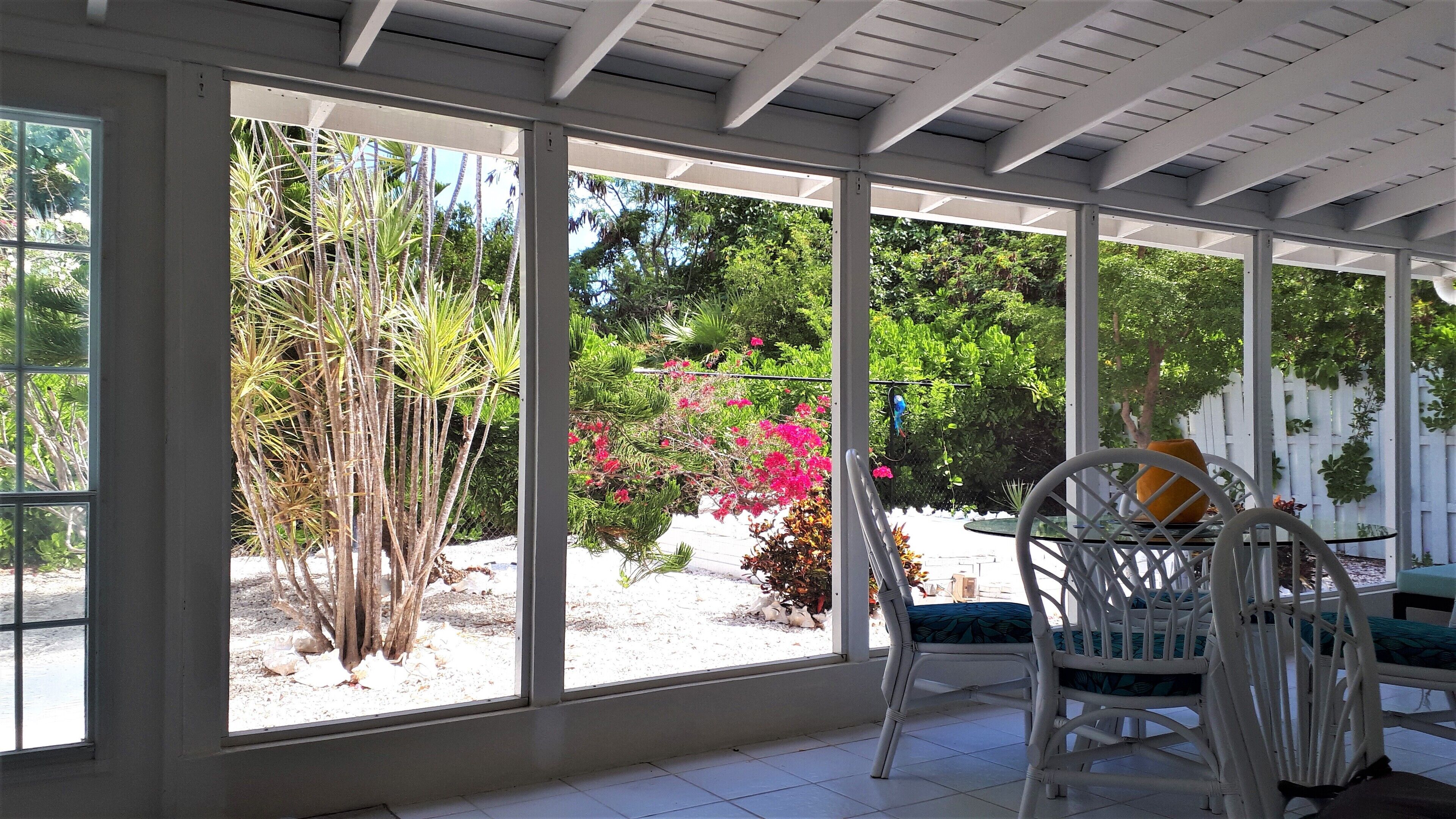 The screened porch with a view of the garden and flowers.