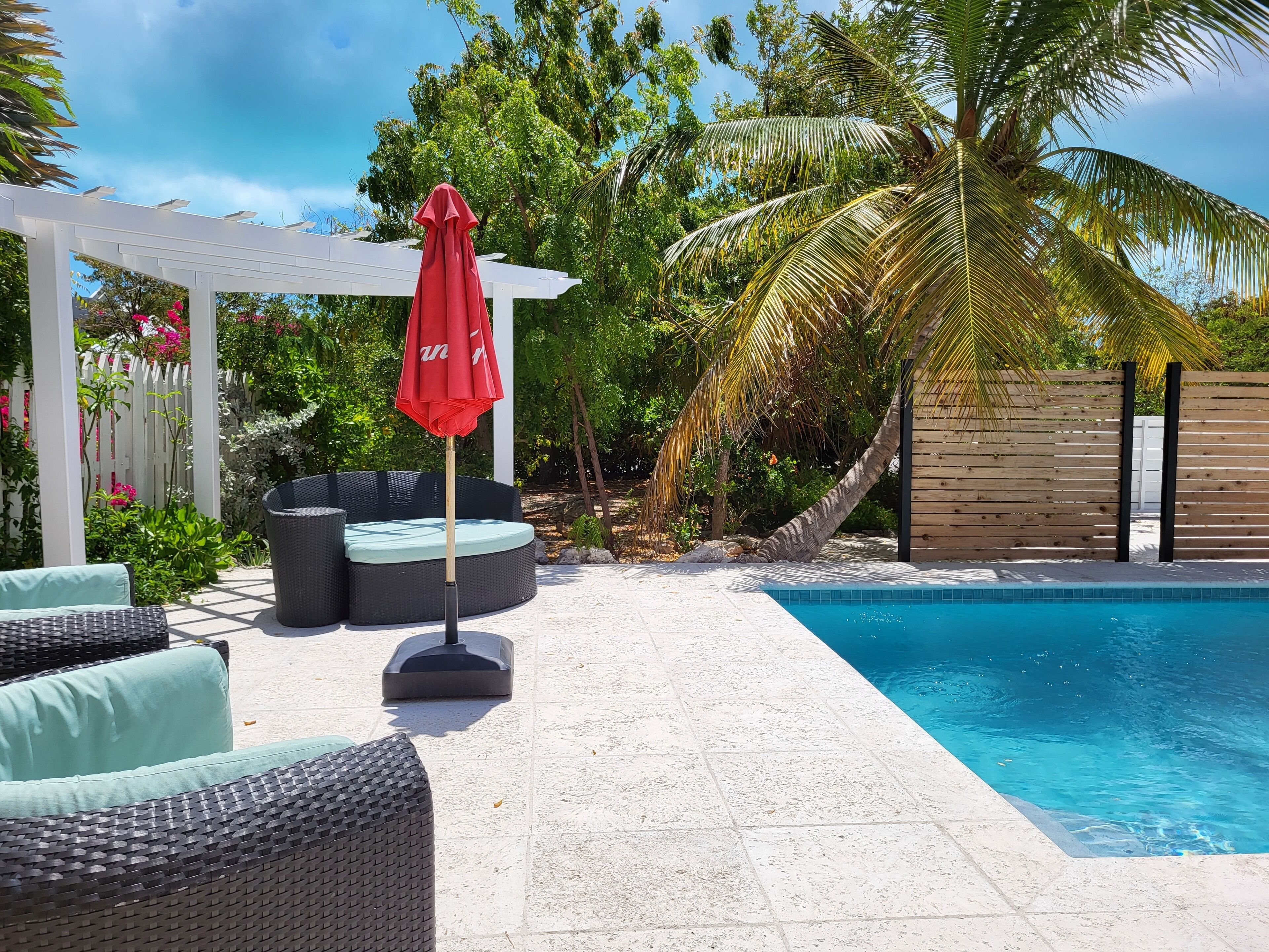 The pool with a red umbrella and a wicker daybed.