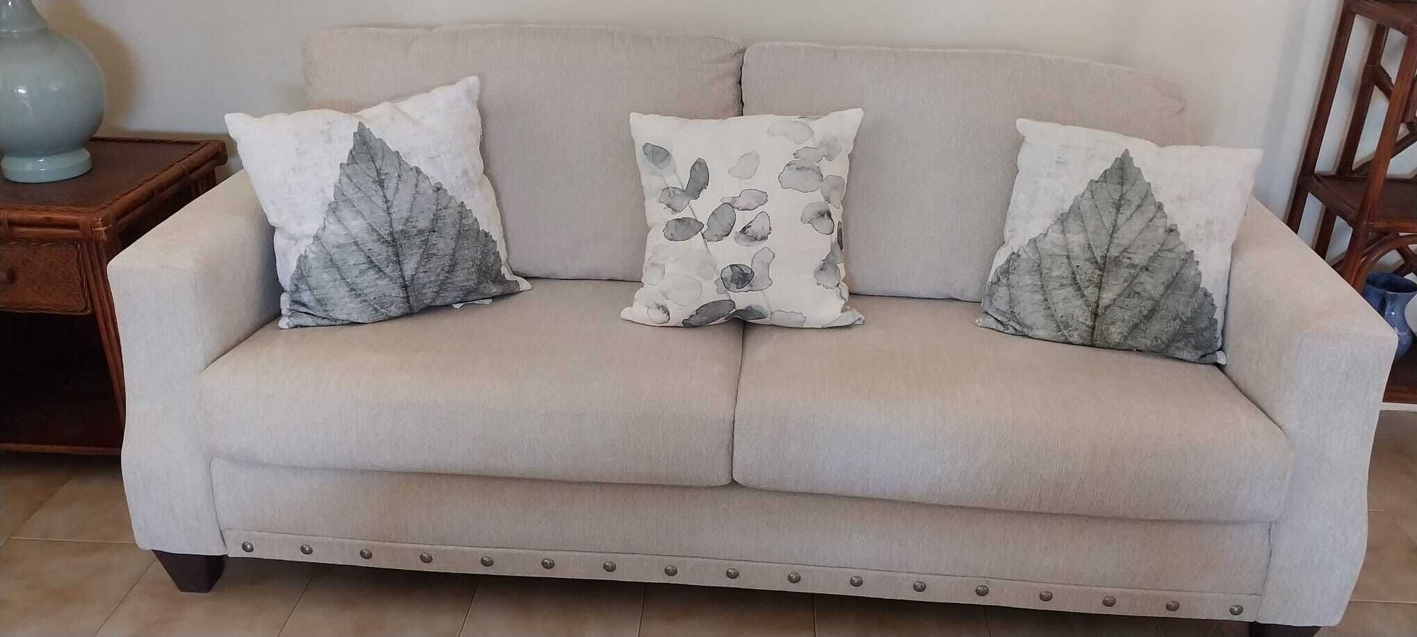A sofa with three leaf-print cushions.