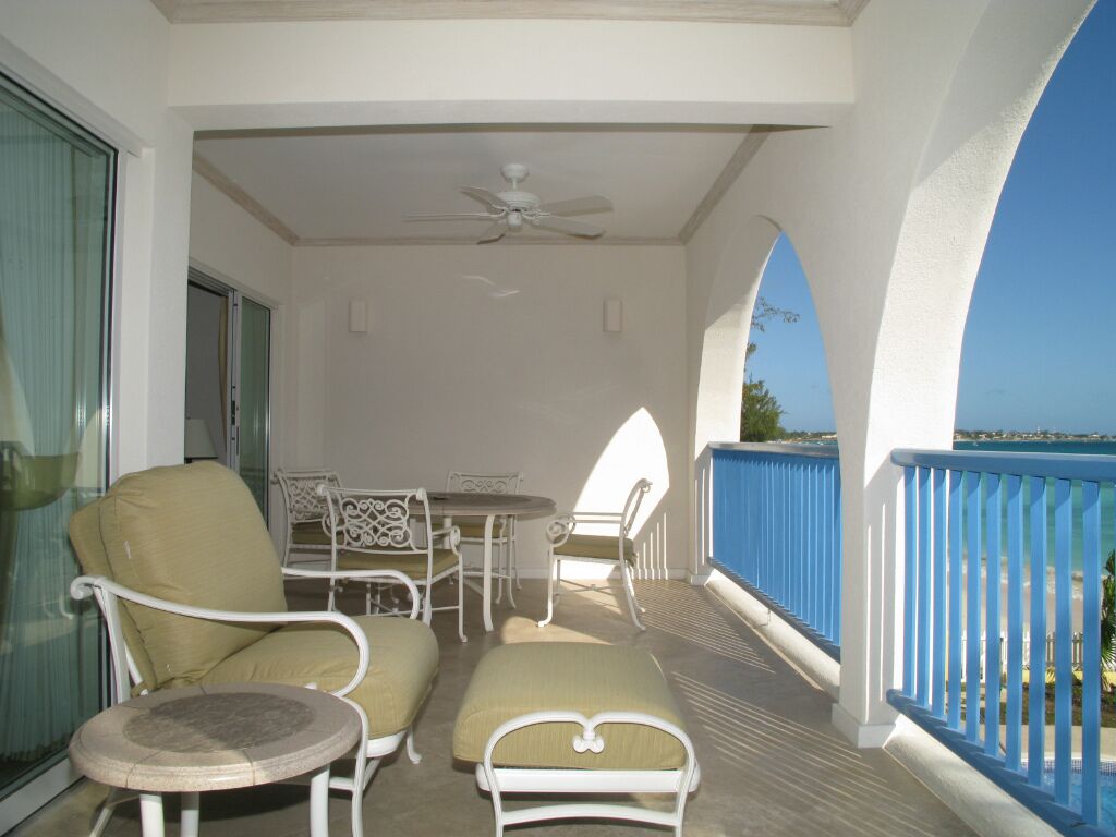 The balcony with a table and seats, with a blue rail and a sea view.