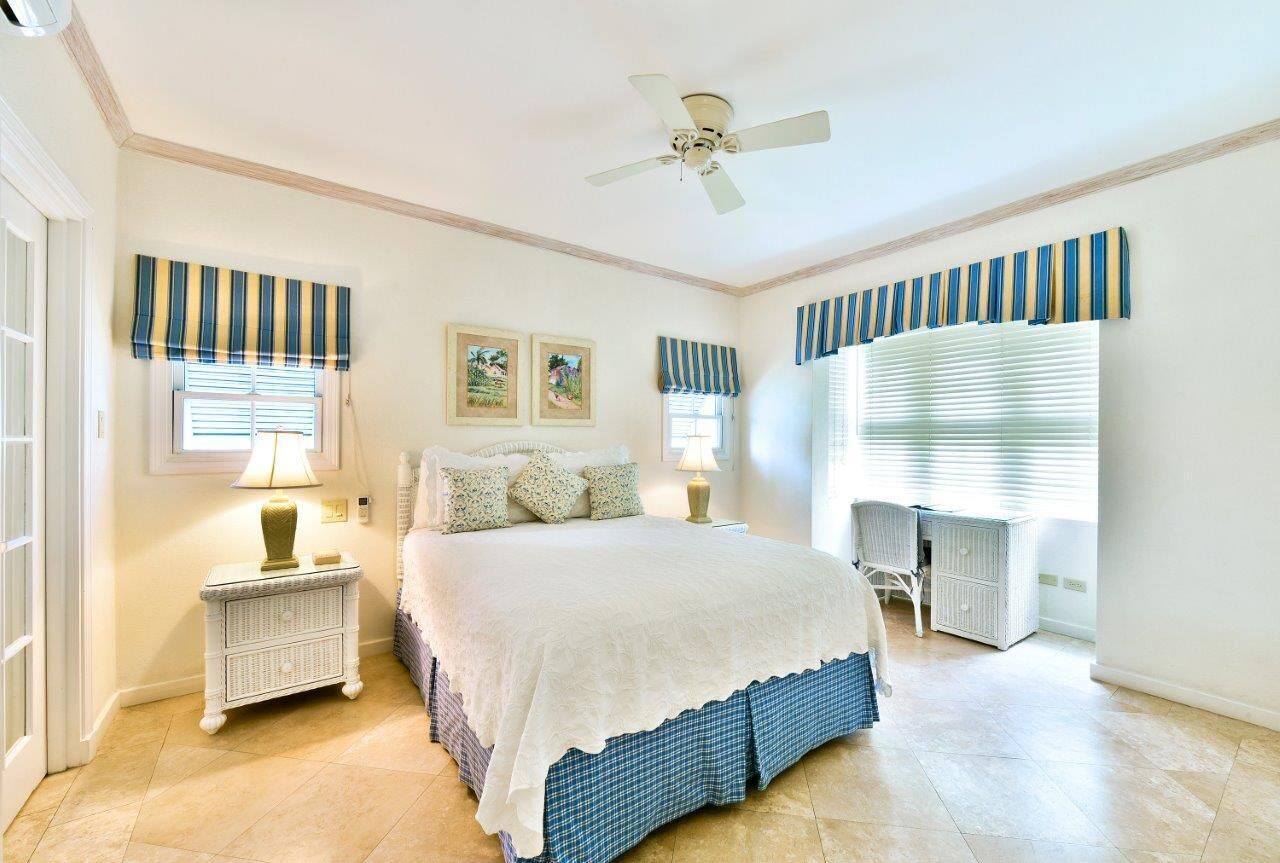 A bedroom with a wide bed, a desk, and striped window blinds.