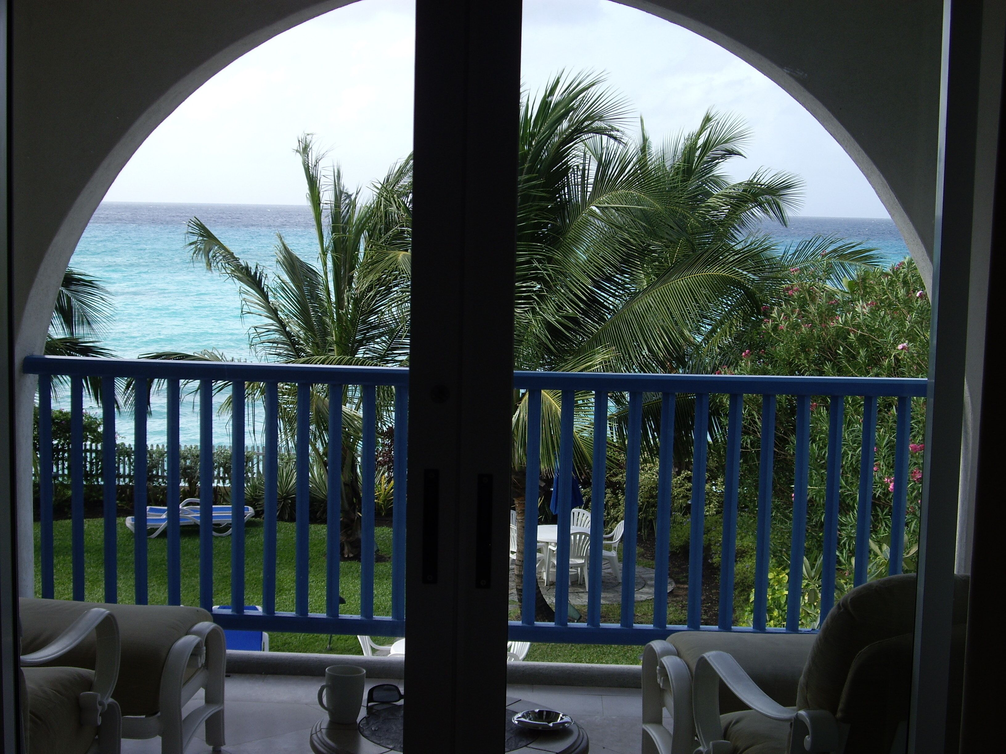 A sea view through the arch of the balcony, with palms below.