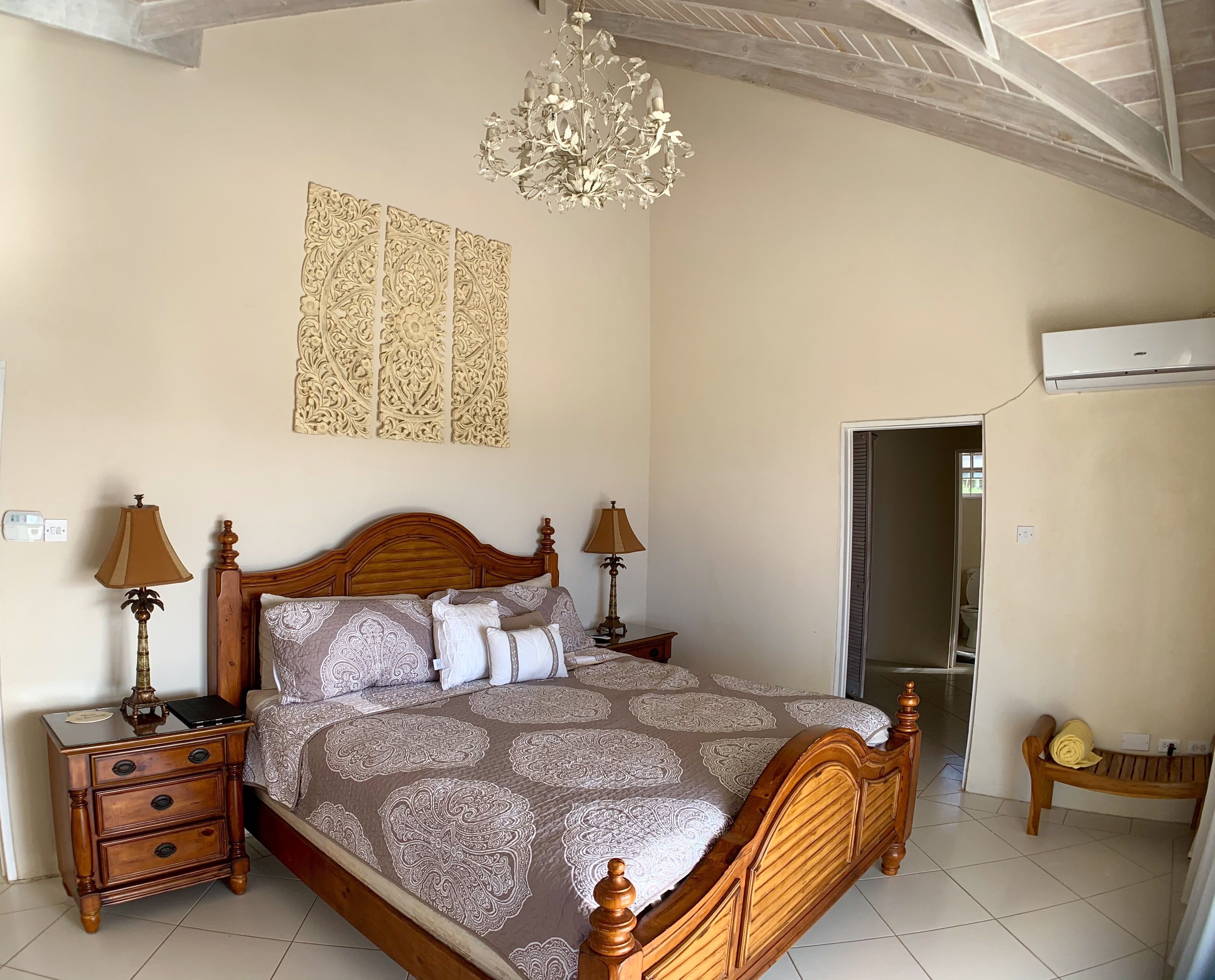 A bedroom with a wooden bed, a patterned bedspread, a chandelier, and an air-conditioning unit.