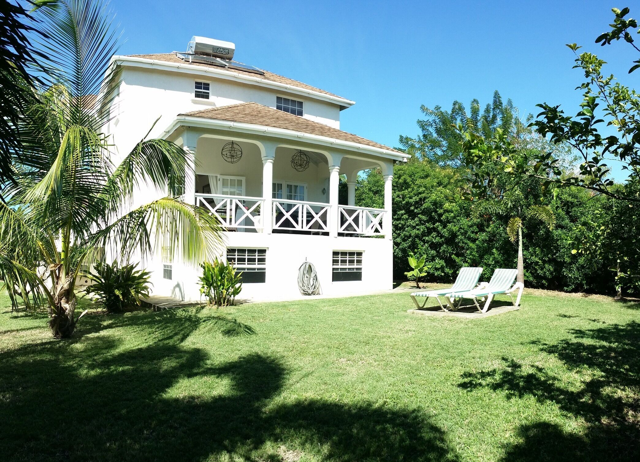 The white two-story villa with a covered veranda, a lawn, and two sun loungers.