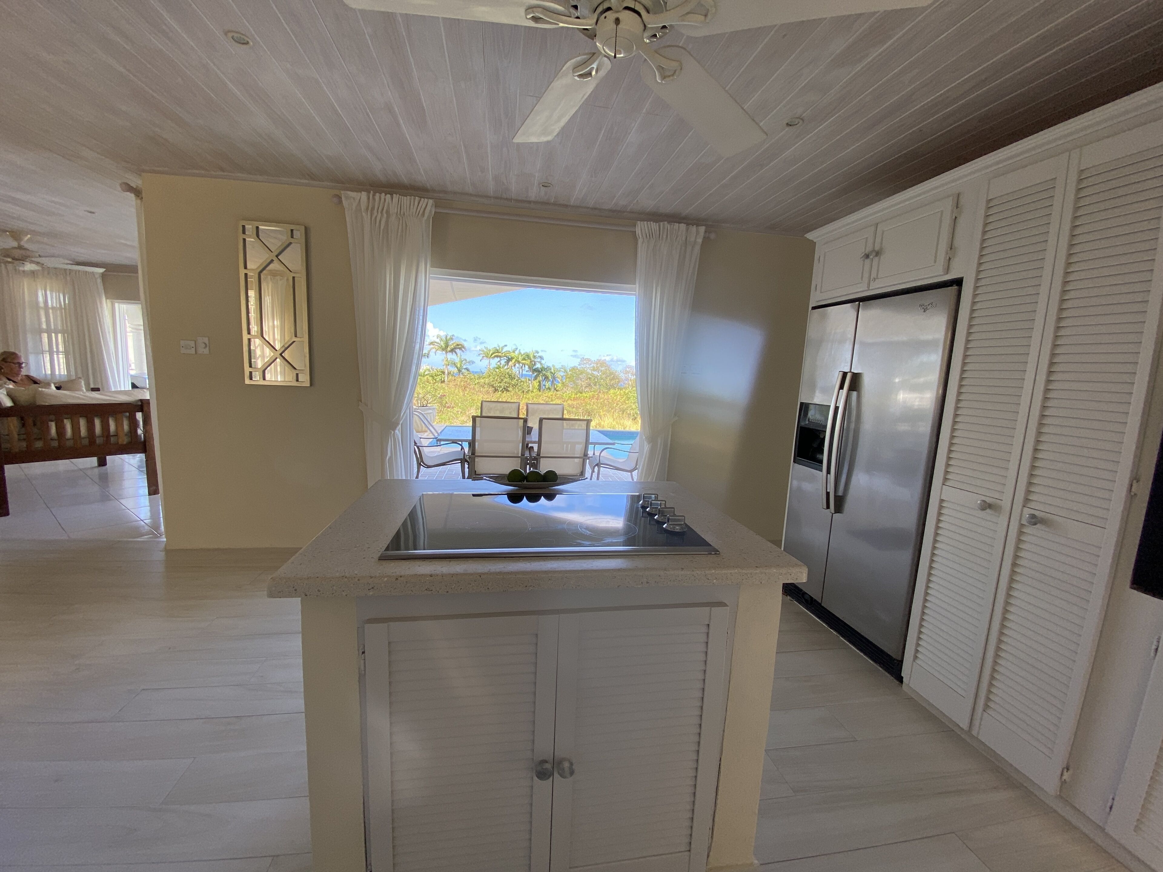 A kitchen island with a cooktop and a view through open doors to the pool terrace and the sea.