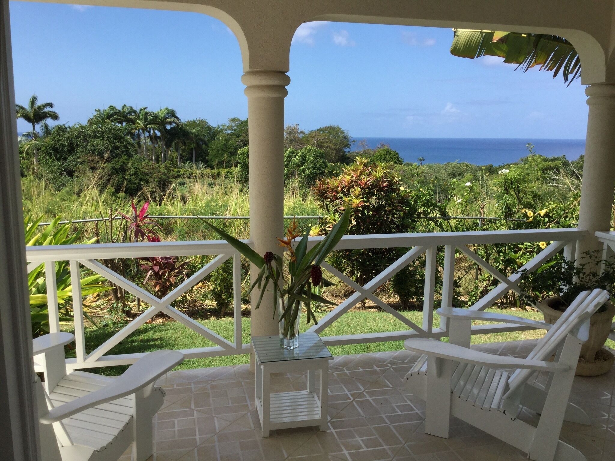 The covered veranda with two white chairs, a side table, and a view of the garden and the sea.