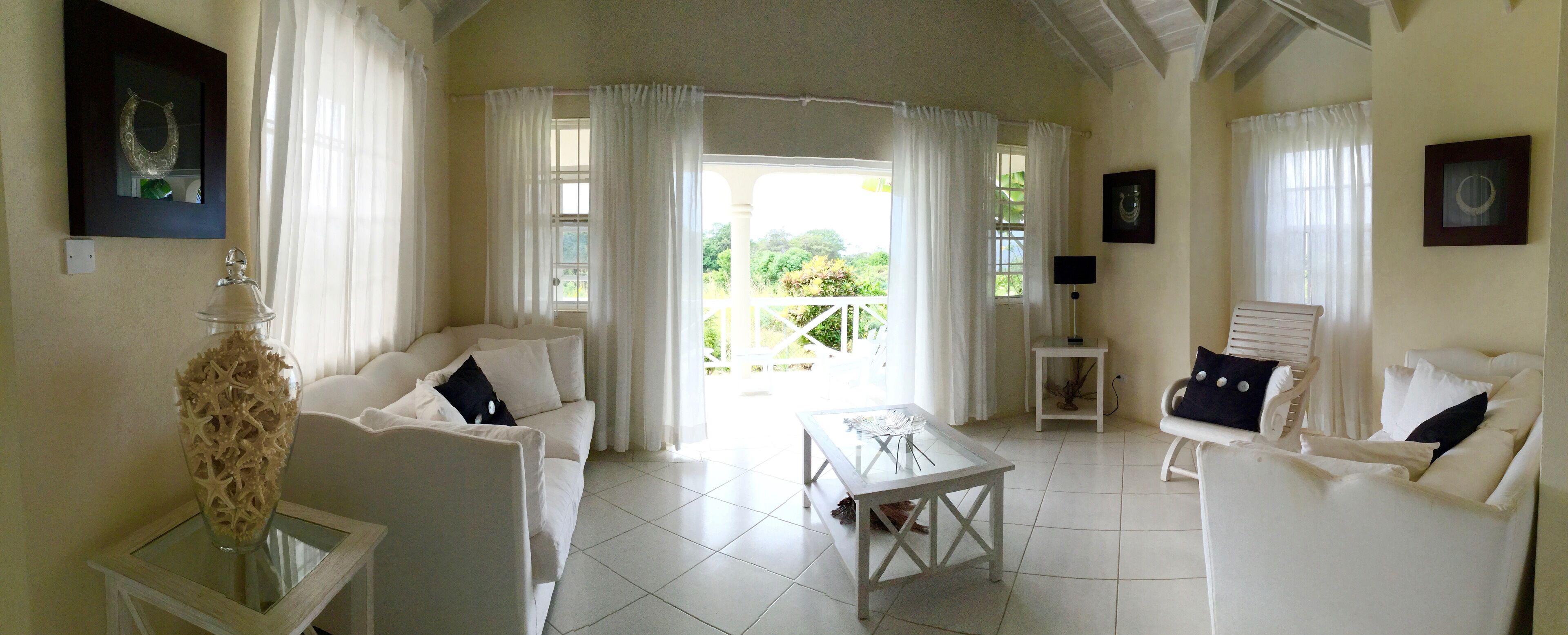 A living room with white sofas, a glass coffee table, and open doors to the veranda.