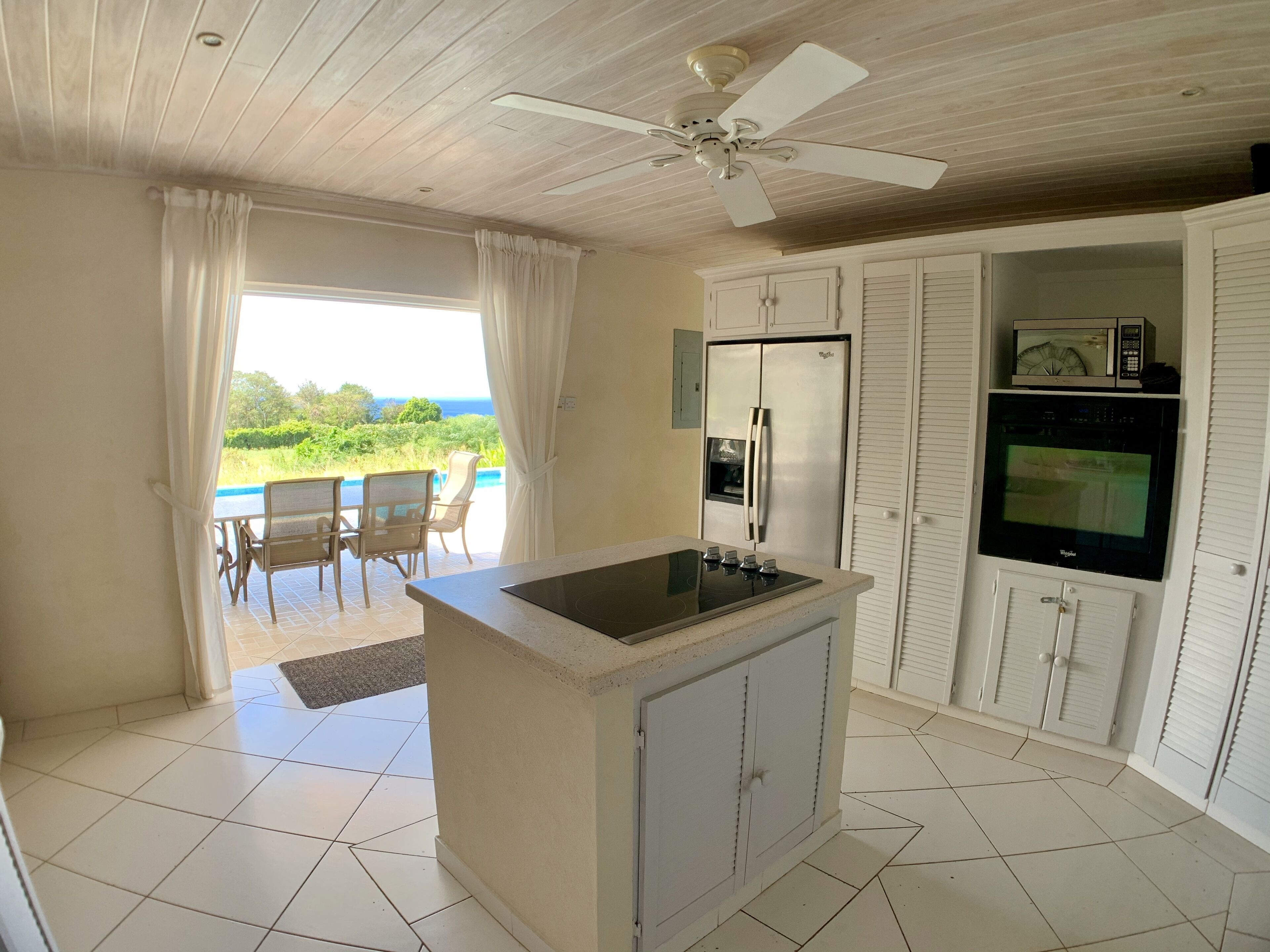 The kitchen with an island cooktop, a wall oven, and open doors to the pool terrace.