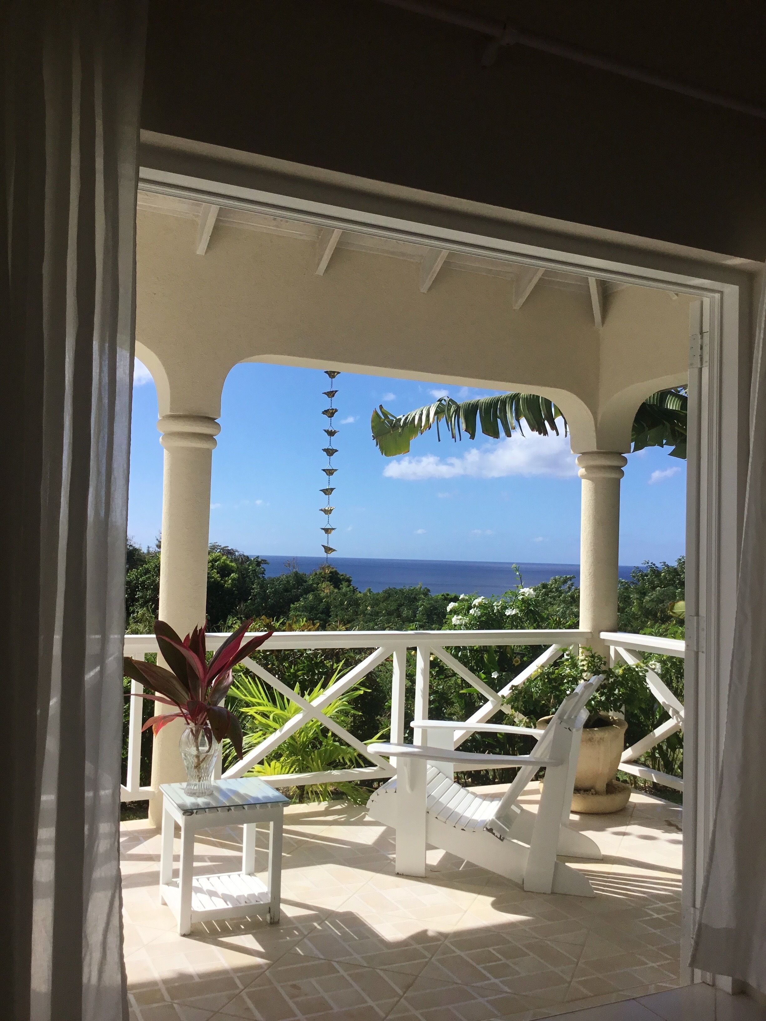 A view through open doors to the balcony with a white chair and the sea beyond.