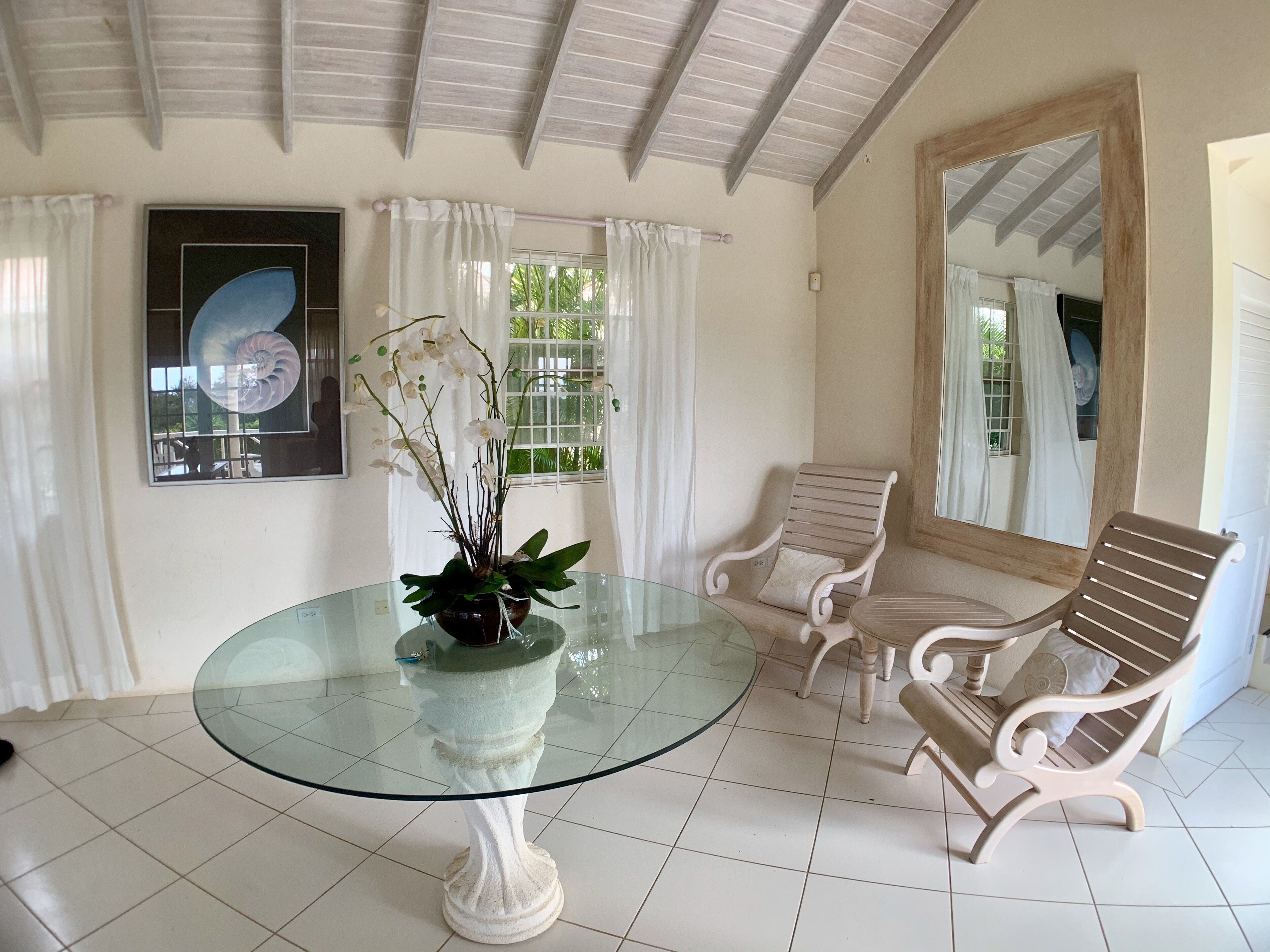 A room with a round glass table, an orchid, two wooden chairs, and a large mirror.