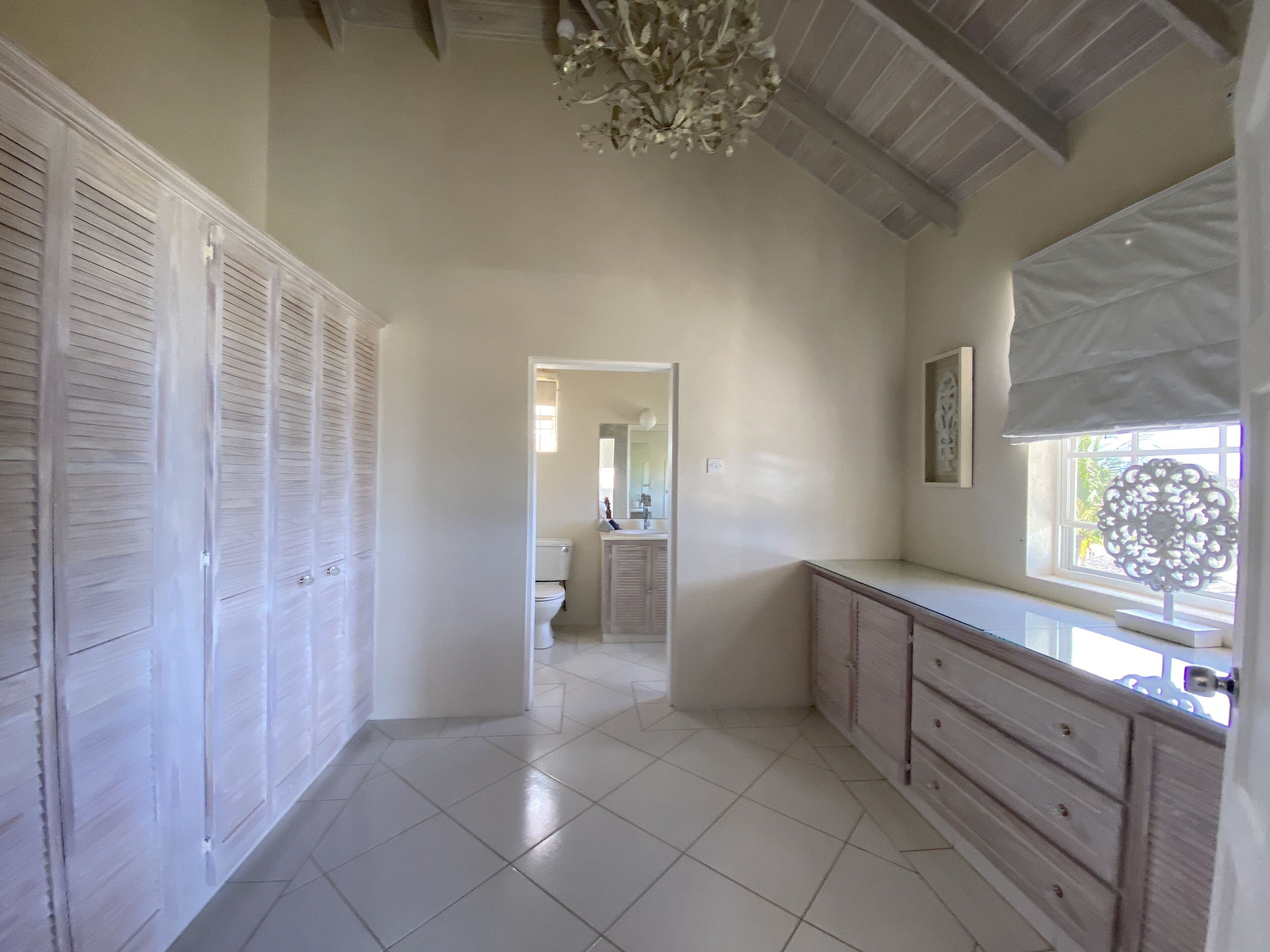 A dressing room with louvered wardrobes, a chest of drawers, and a door to a bathroom.