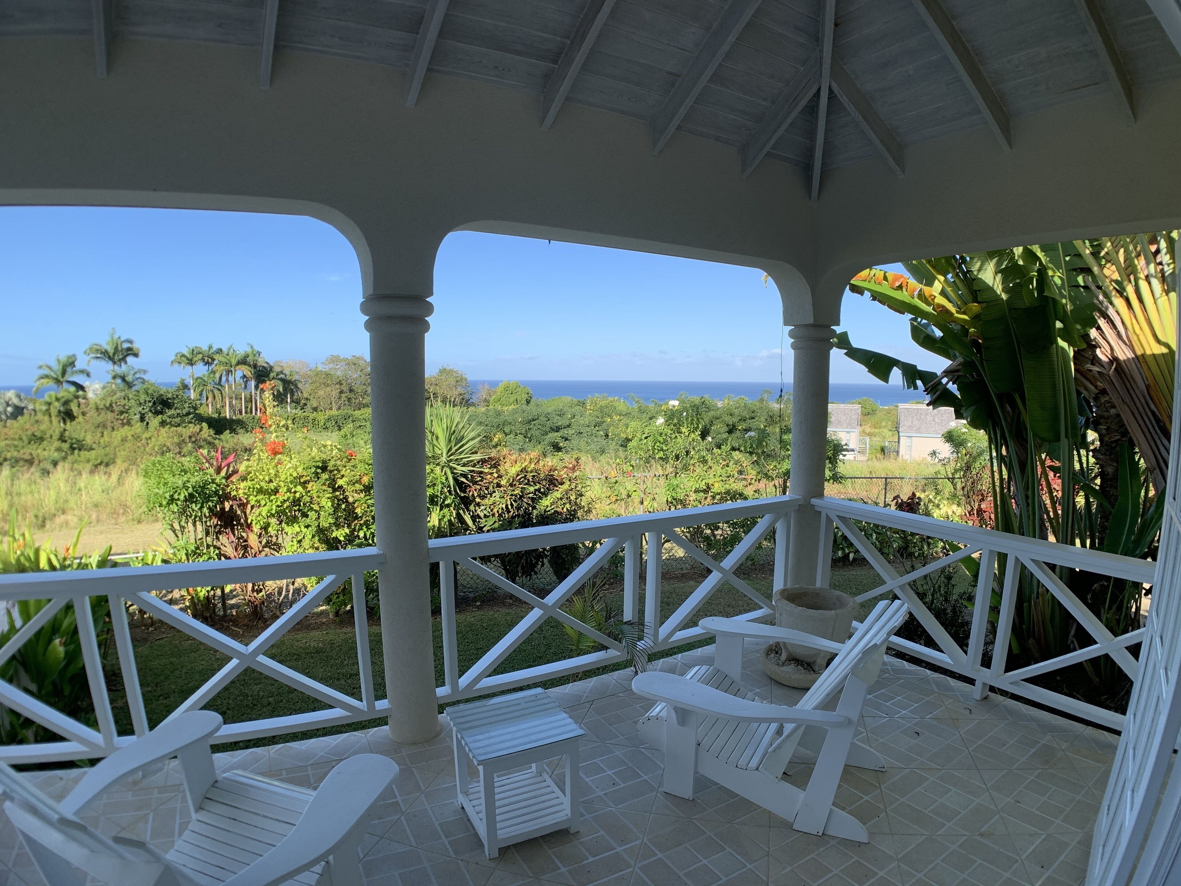 The covered veranda with white chairs and a view over the garden to the sea.