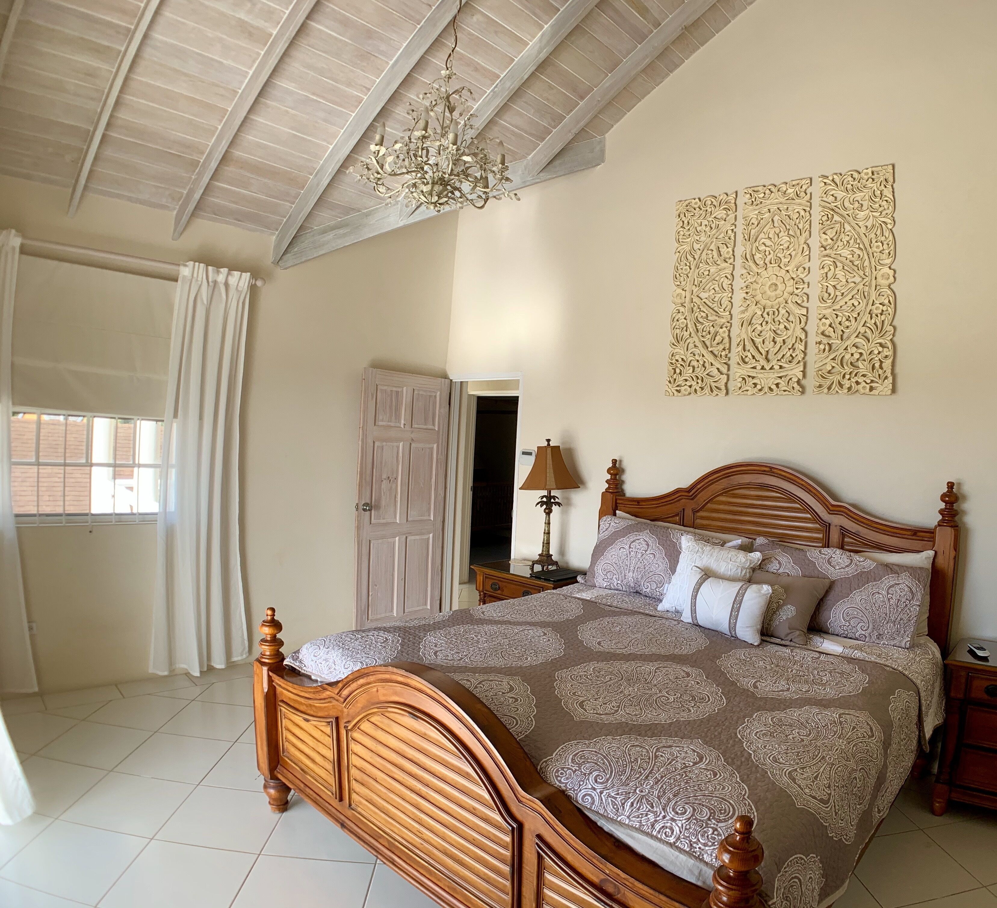 A bedroom with a wooden bed, a patterned bedspread, carved wall panels, and a chandelier.