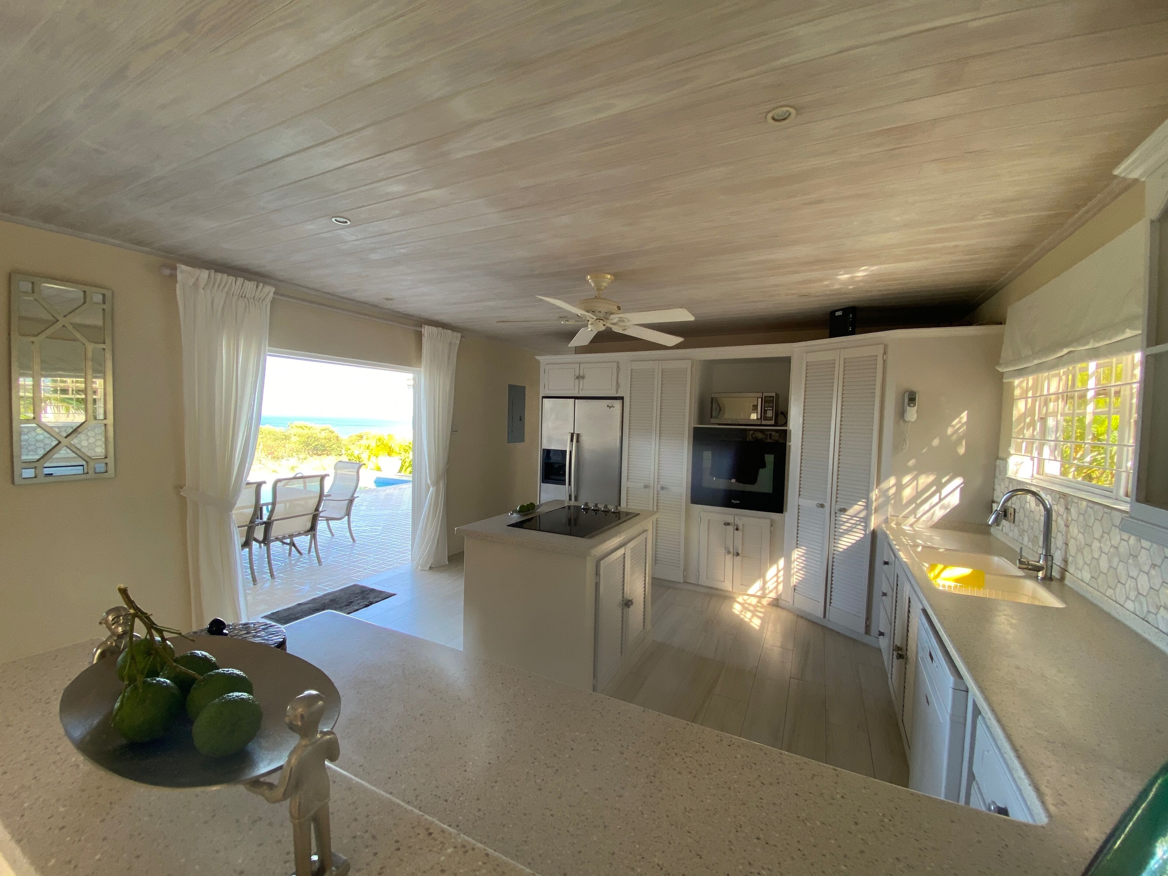 The kitchen with an island cooktop and open doors to the pool terrace and the sea.