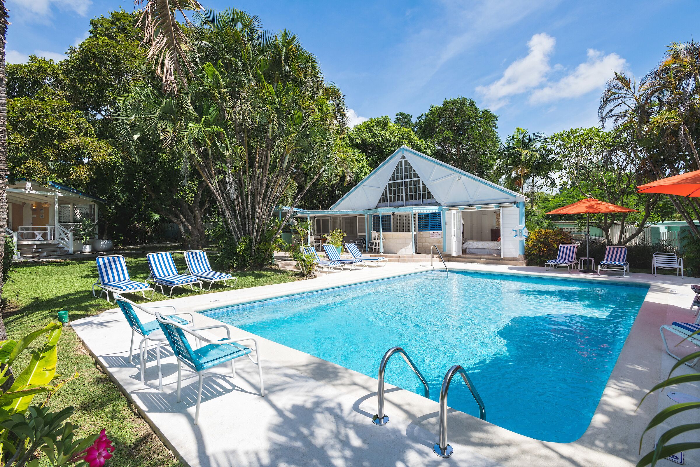 The pool, sun loungers, and the pool cottage under a blue sky.