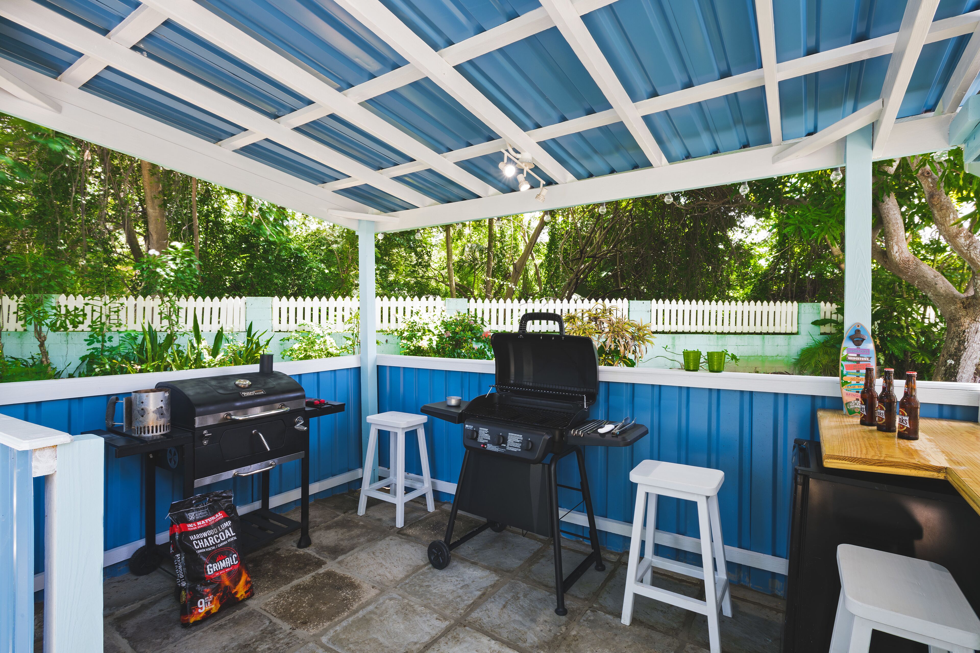 A covered barbecue hut with two grills, white stools, and a bar counter.