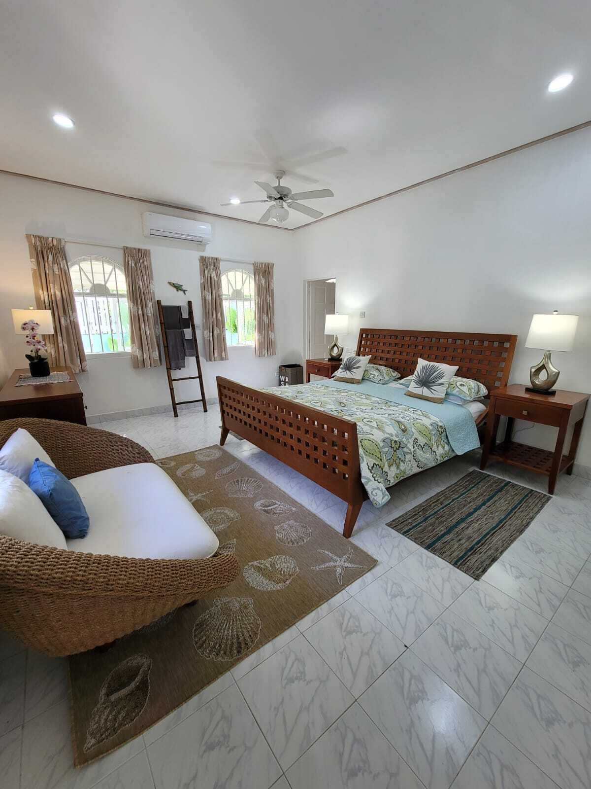 A bedroom with a wood king bed, two lamps, and a wicker seat.