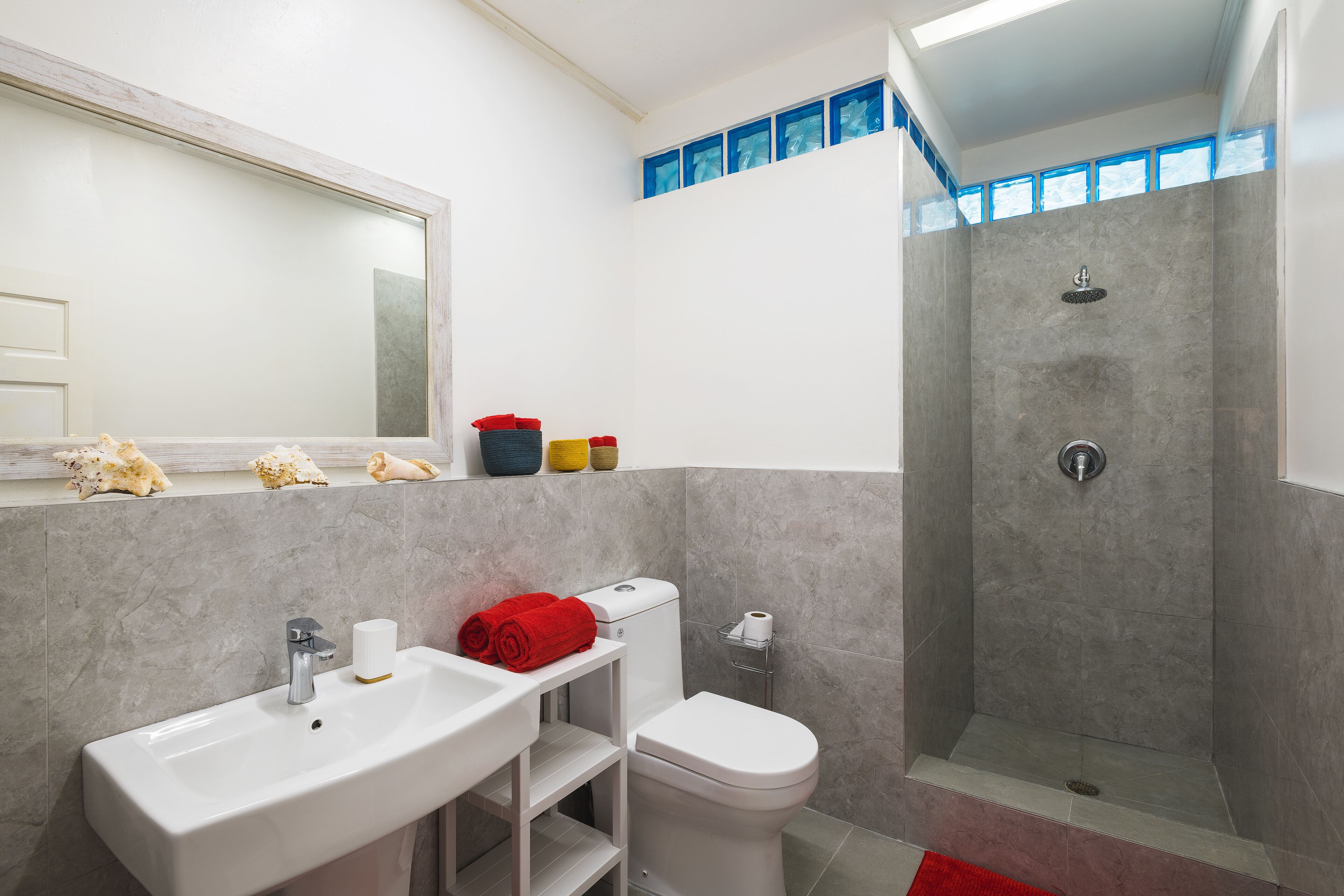 A bathroom with gray tiles, a shower, and red towels.