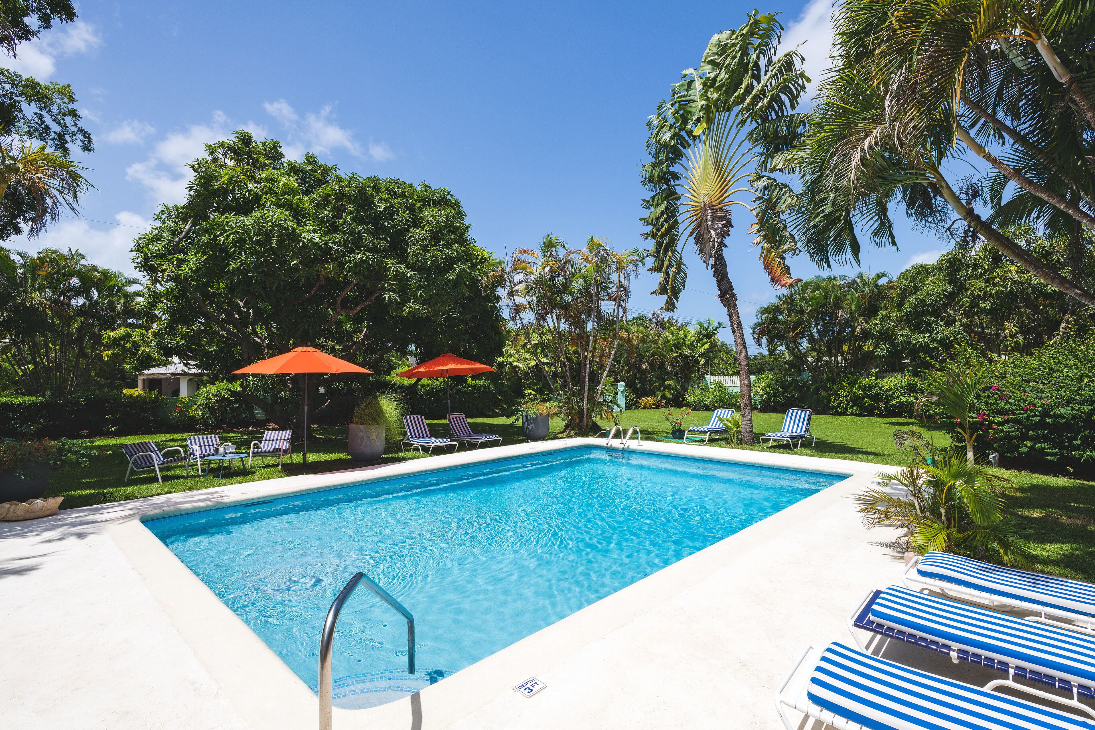 The pool with a ladder, sun loungers, and two orange umbrellas.