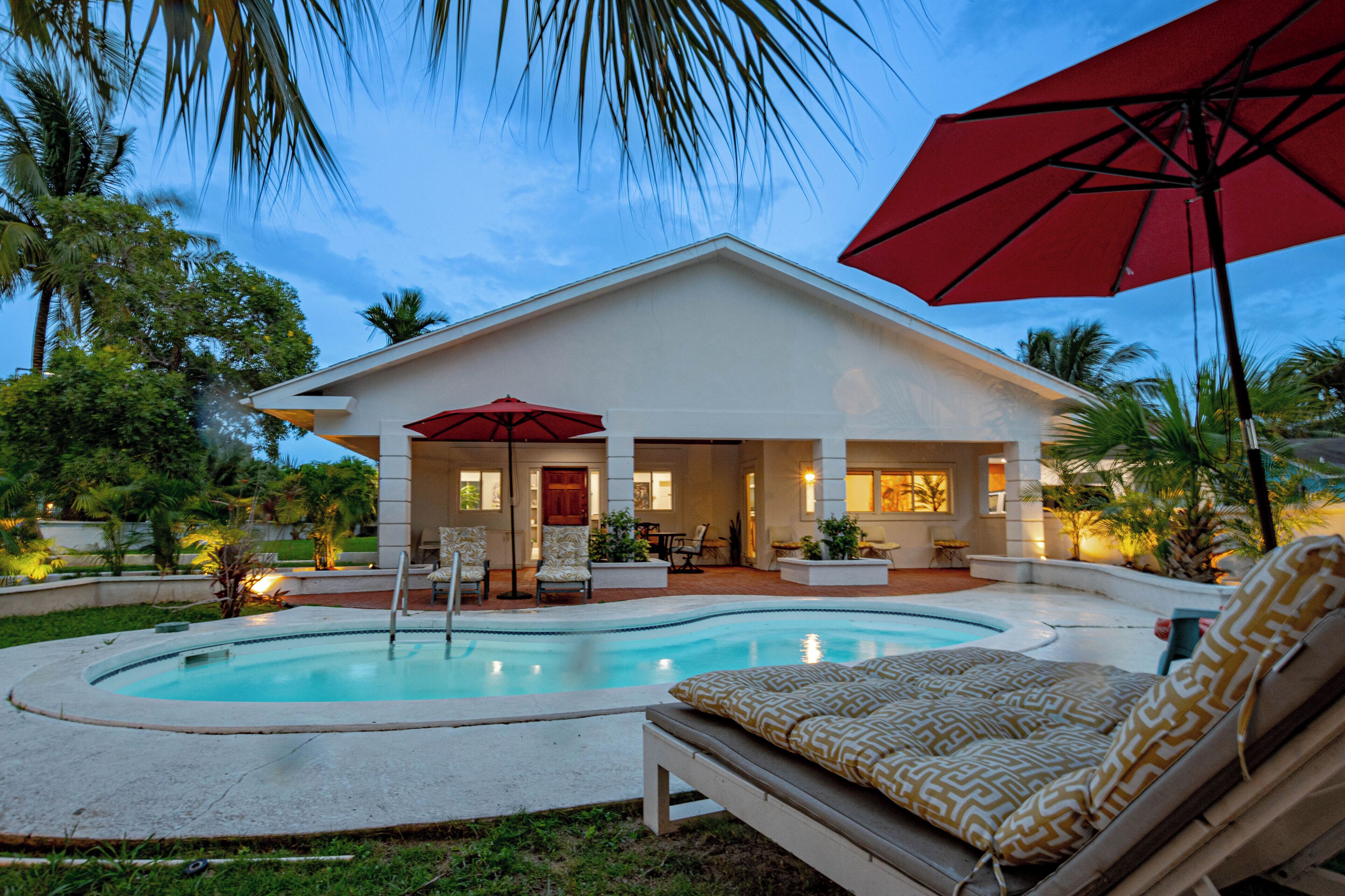The house, the pool, and a red umbrella at dusk.