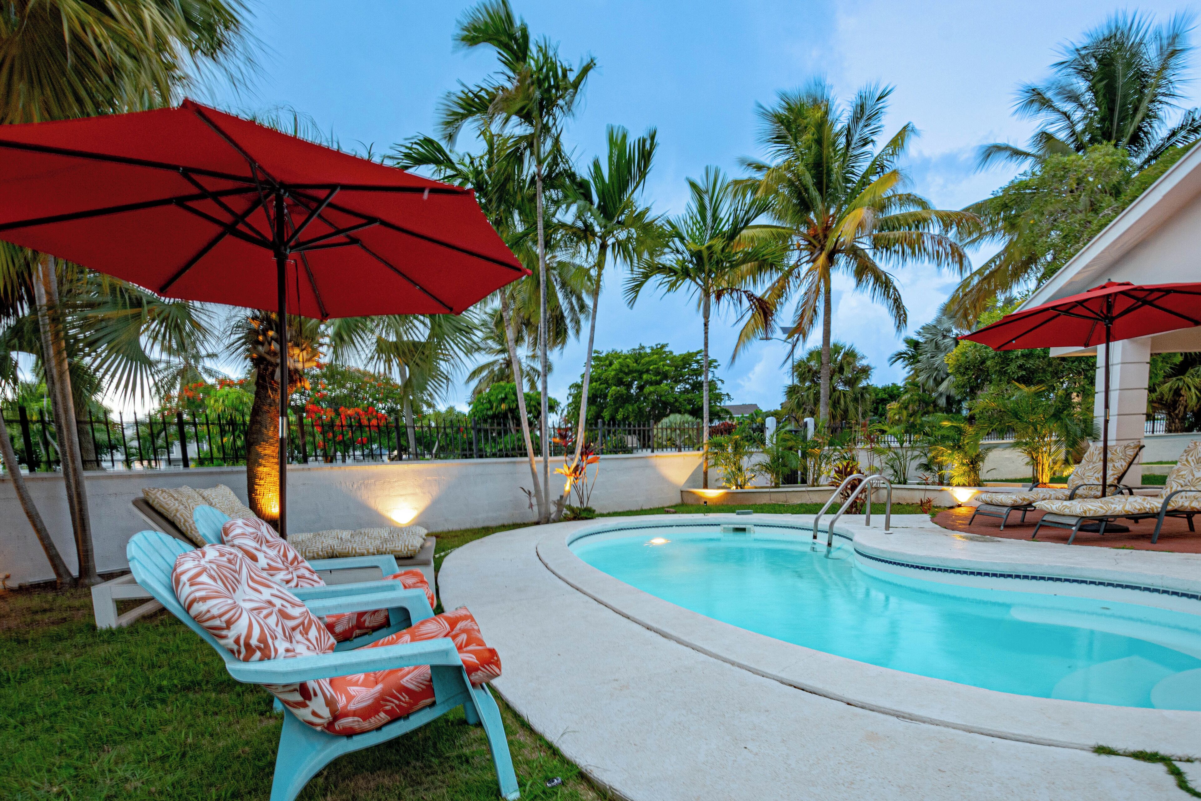 Chairs with cushions and a red umbrella next to the pool.