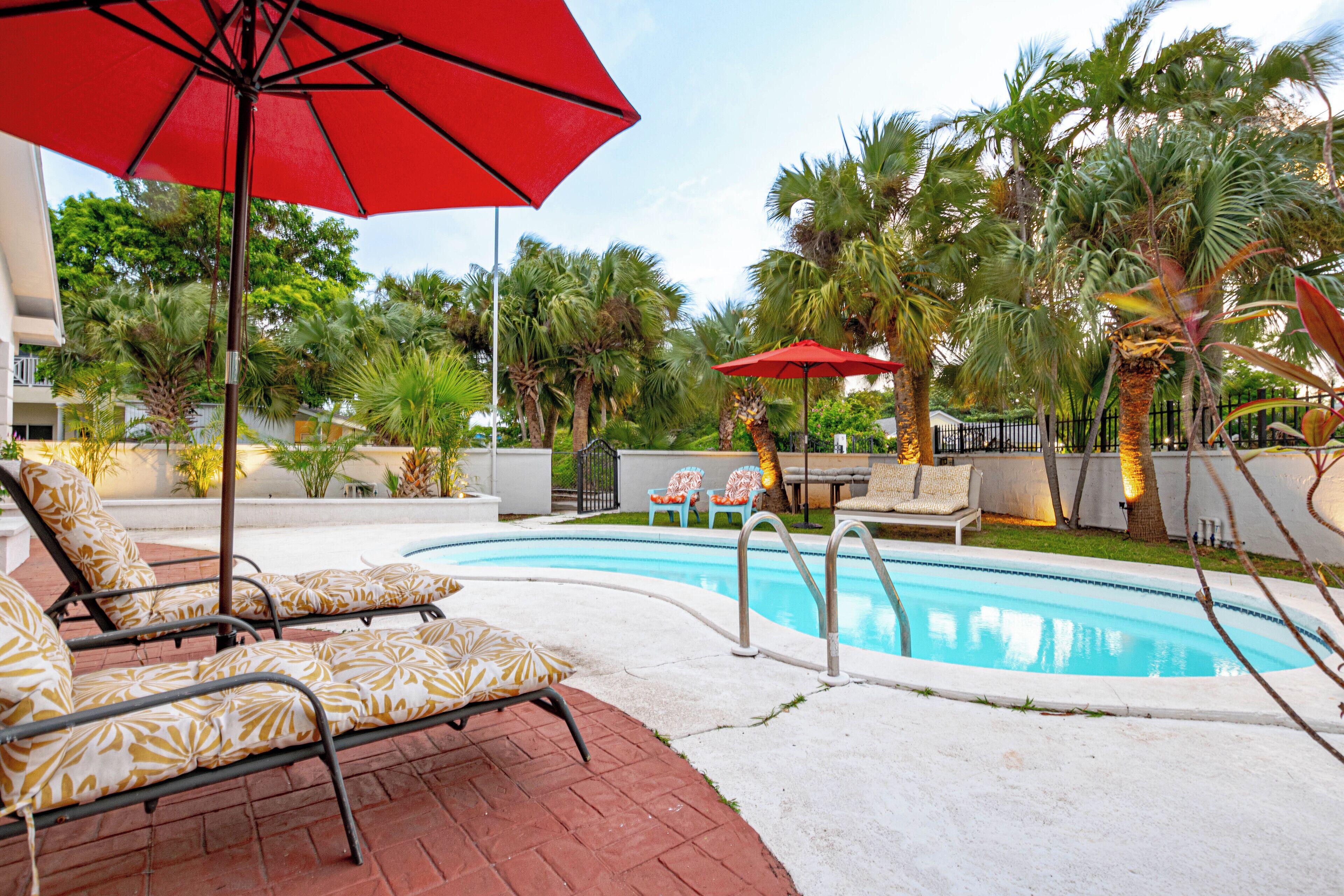 Two lounge chairs under a red umbrella next to the pool.