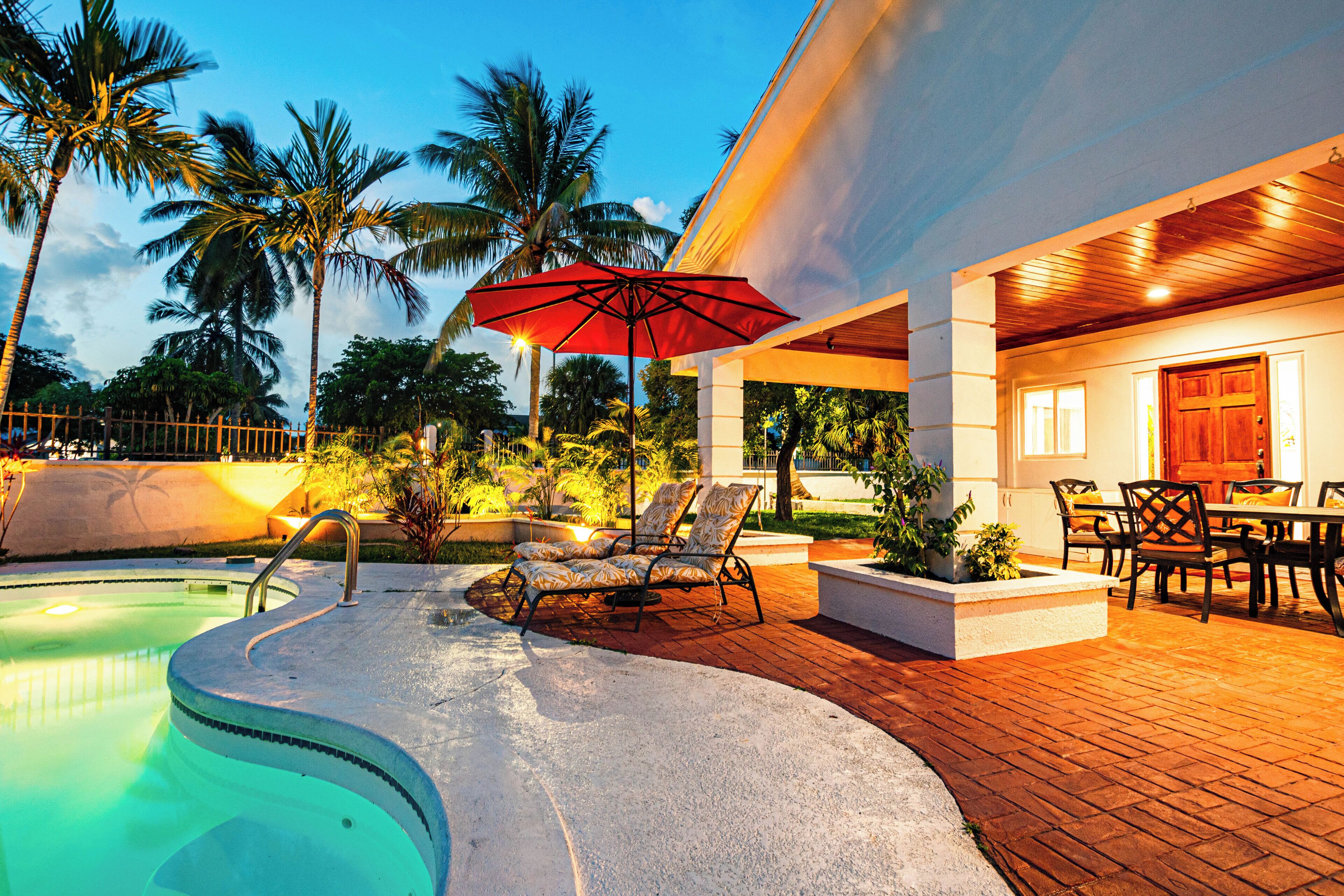 Lounge chairs under a red umbrella between the pool and the patio.