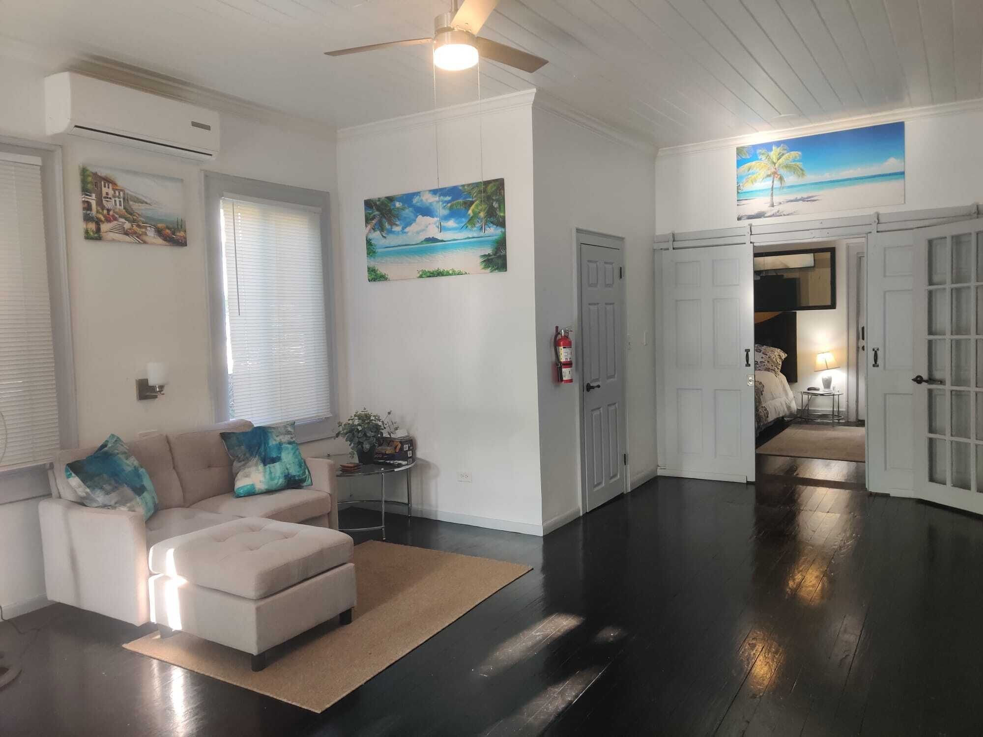 A living room with a sofa, a ceiling fan, and dark wood floors.